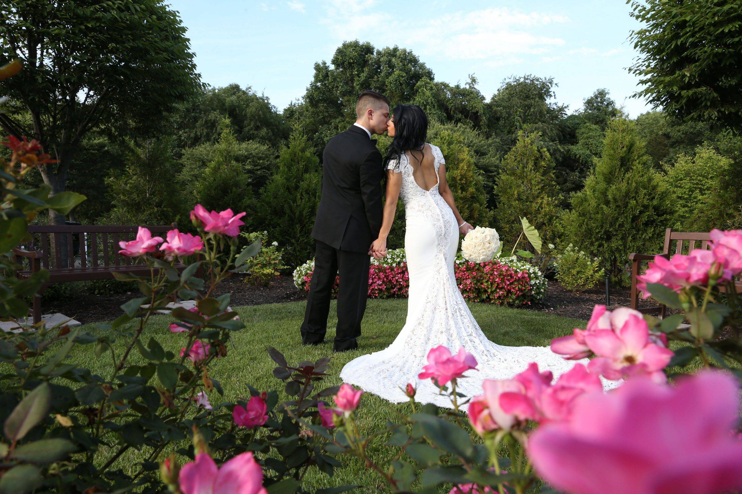 A bride and groom kissing in front of pink flowers.