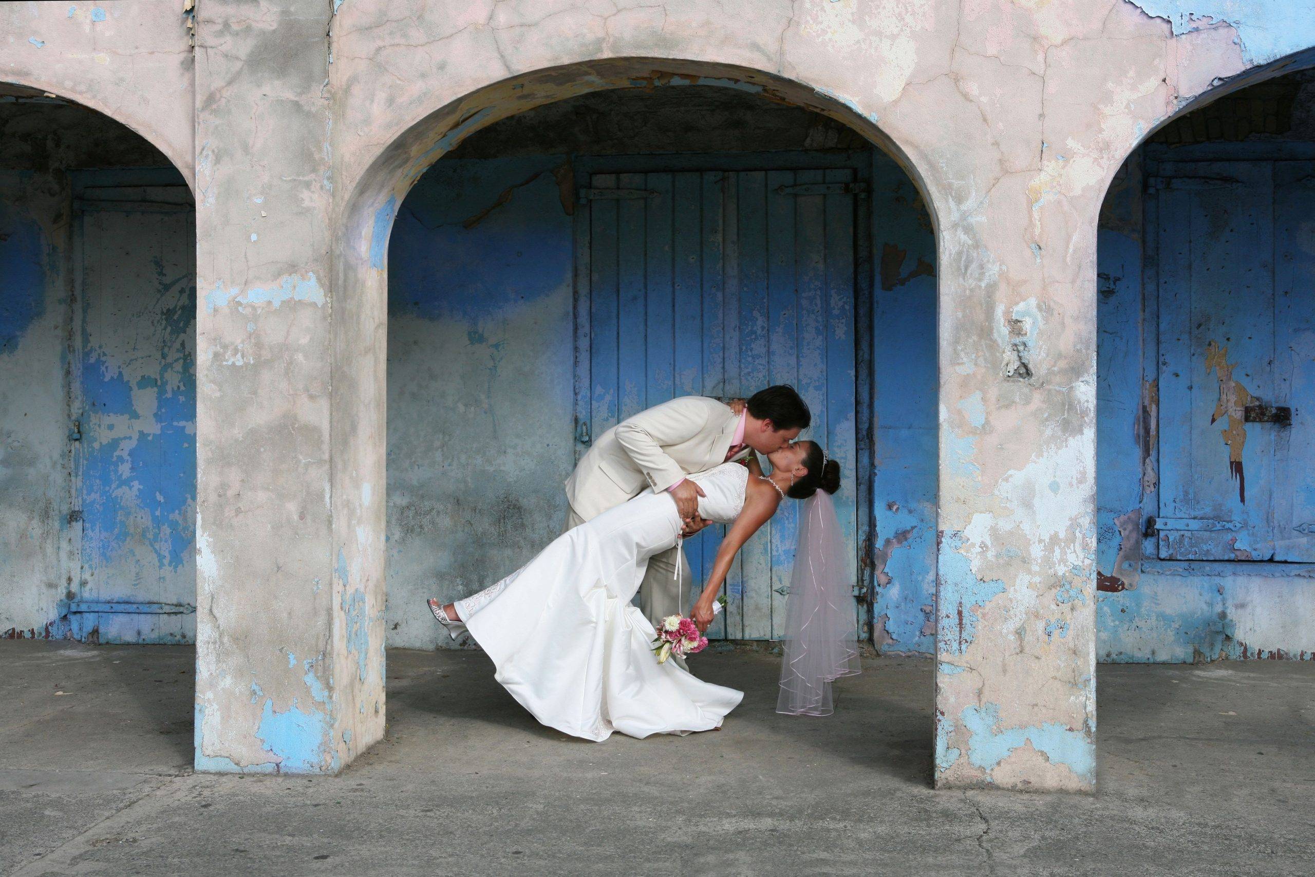 A bride and groom kiss in front of a blue building.