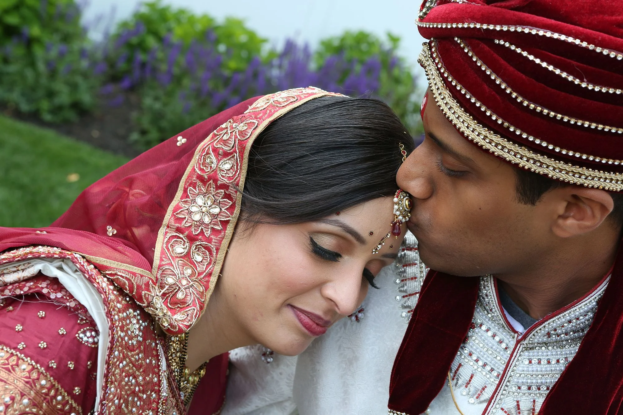 An indian bride and groom kissing on the cheek.