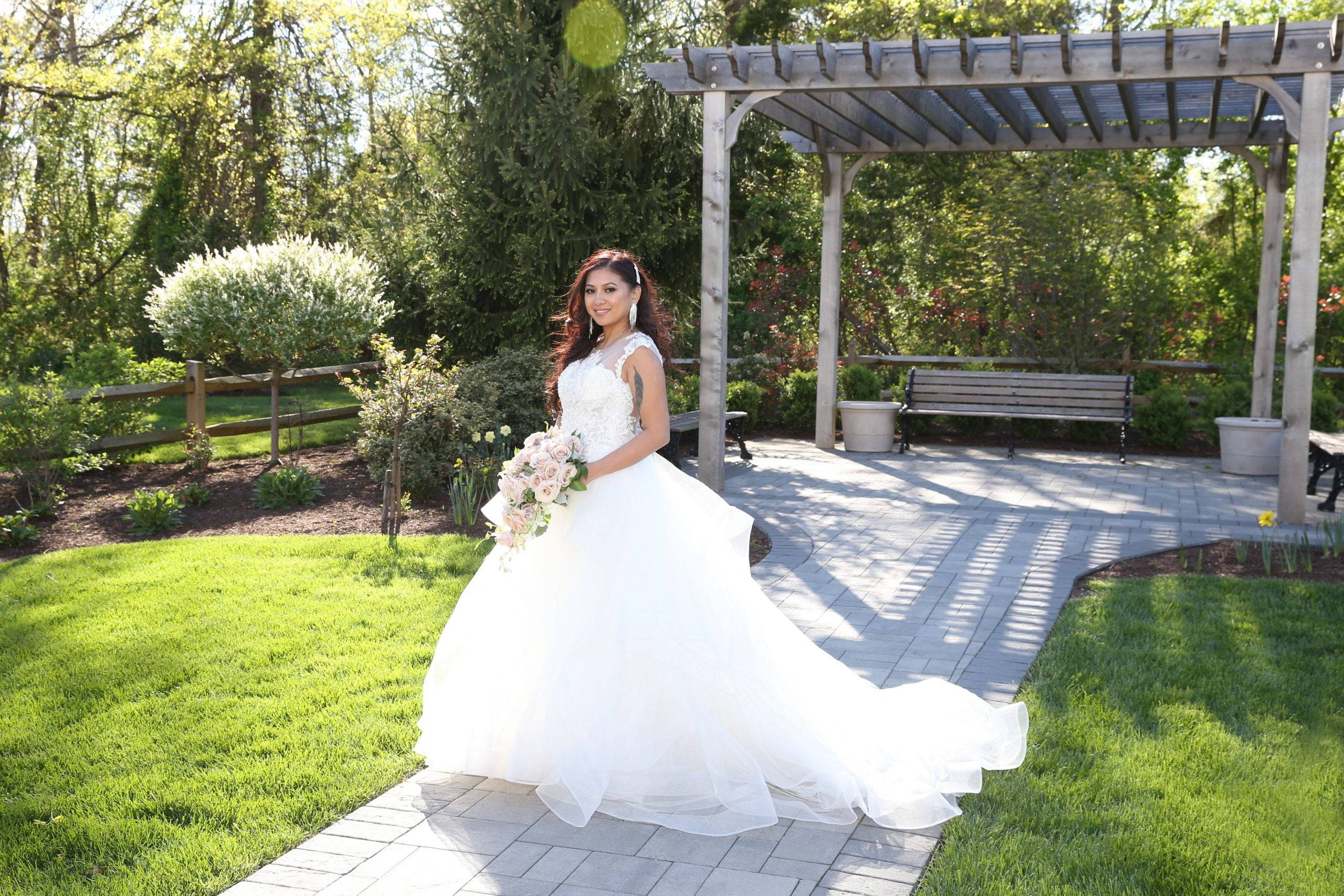 A bride is posing in front of a gazebo in a garden.