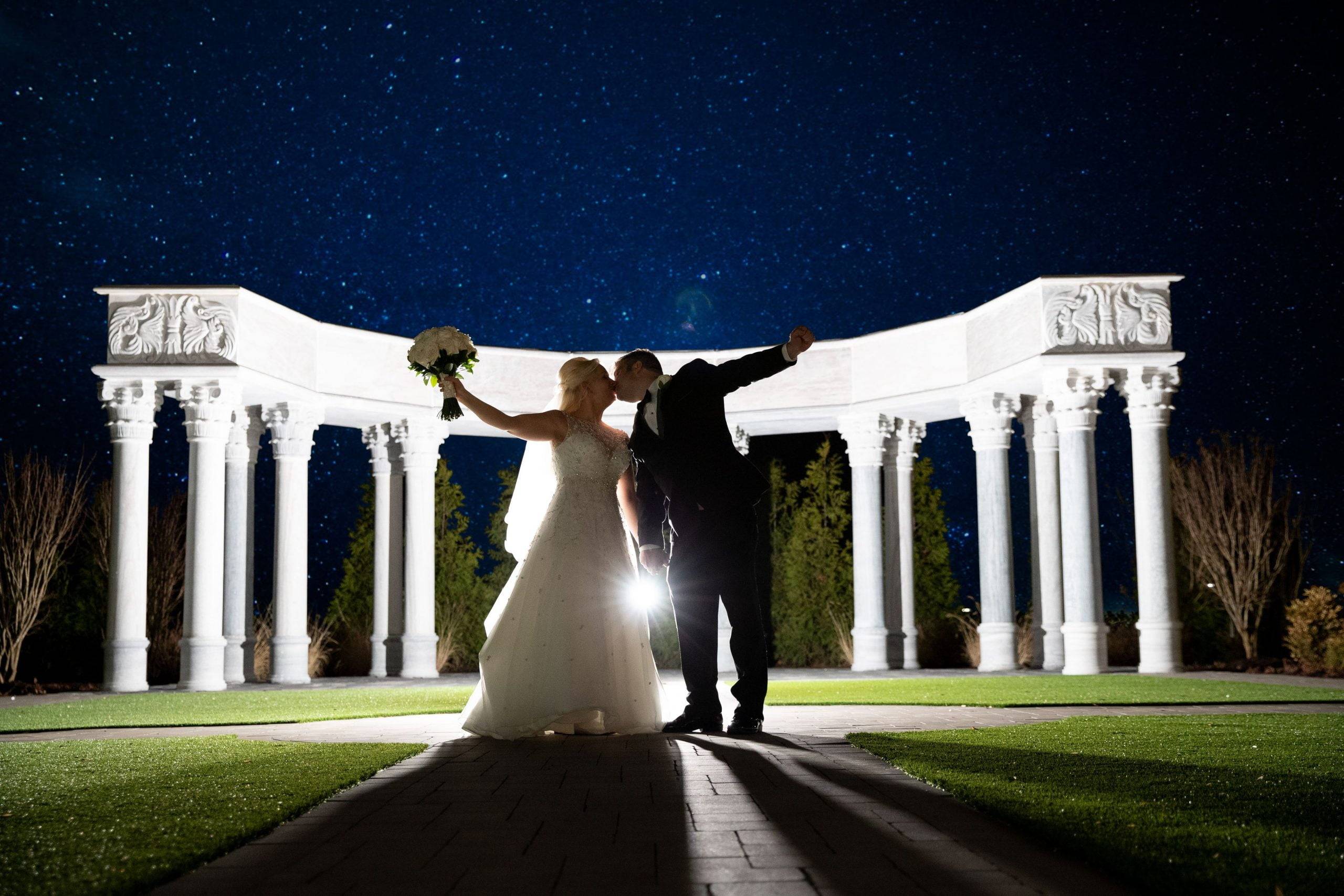 A bride and groom standing in front of a gazebo at night.