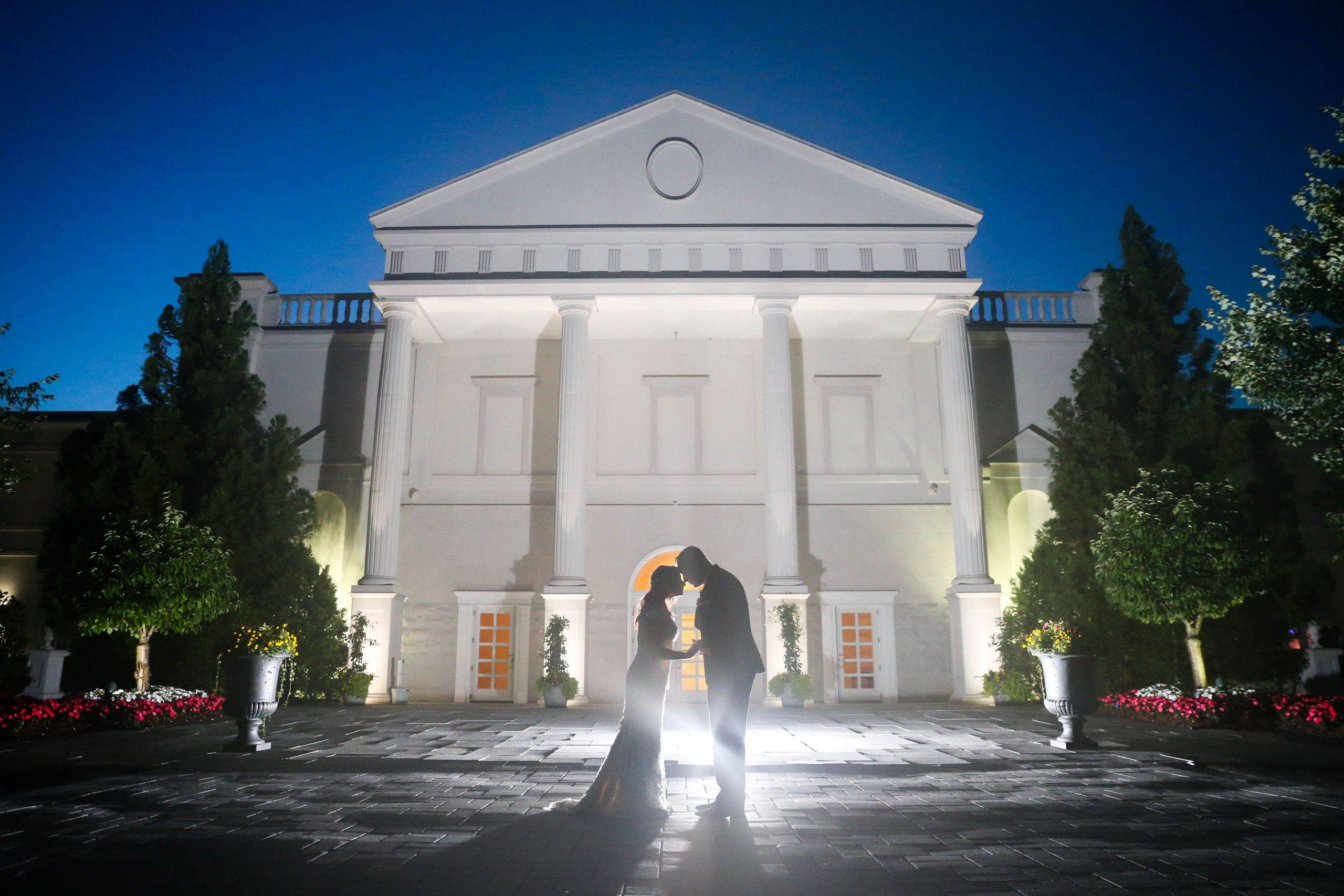 A bride and groom standing in front of a white building at night.