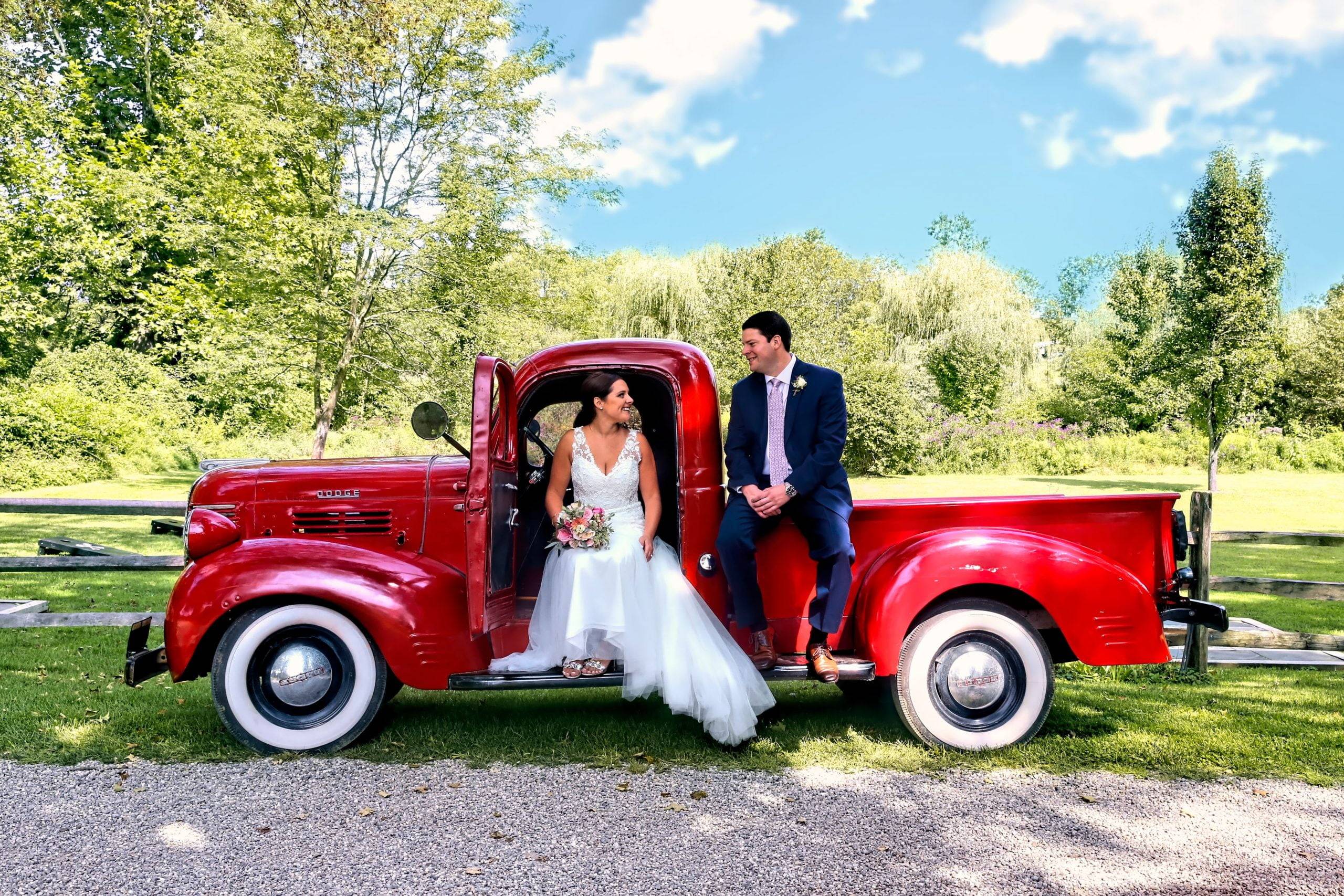 A bride and groom sitting in the back of a red truck.