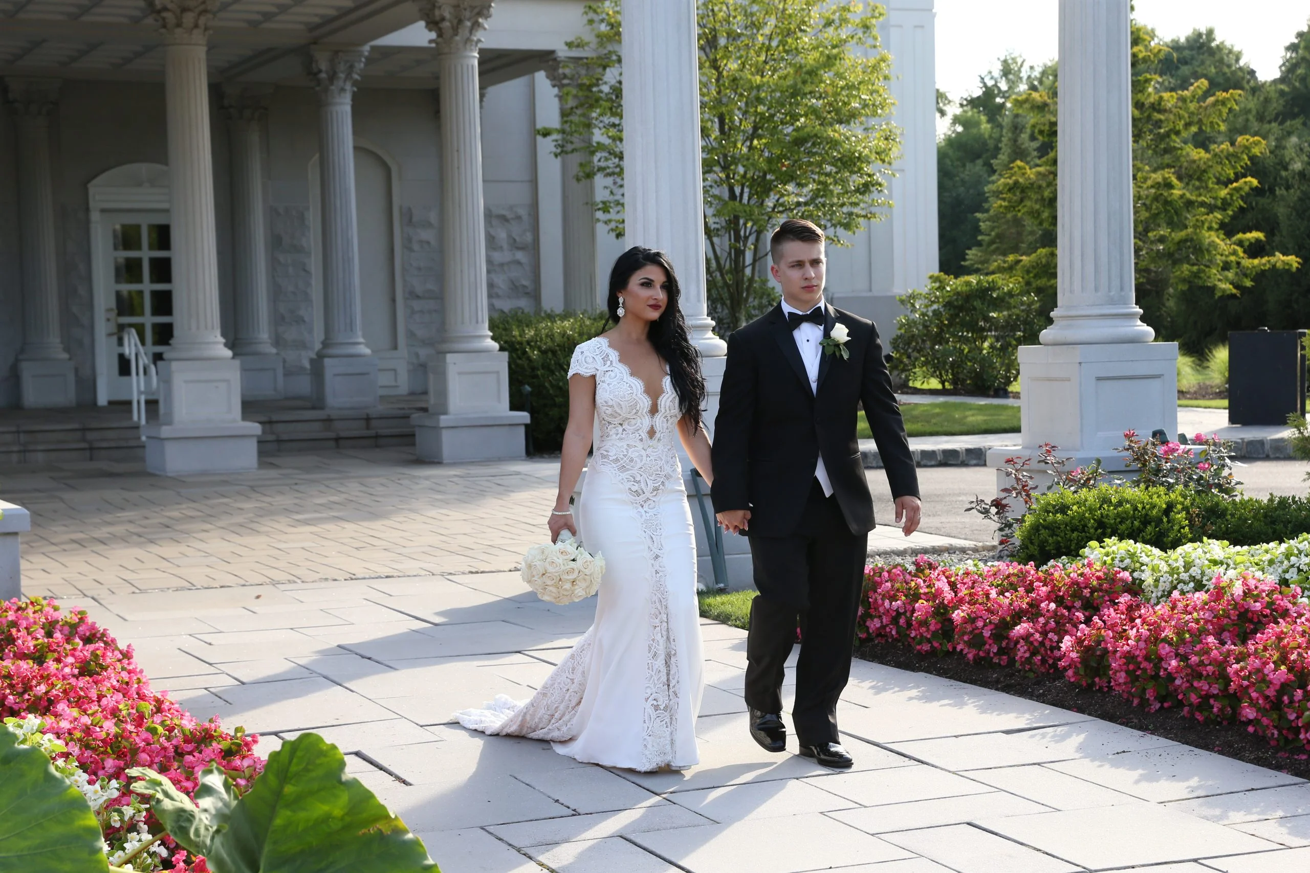 A bride and groom walking down a pathway in front of a mansion.