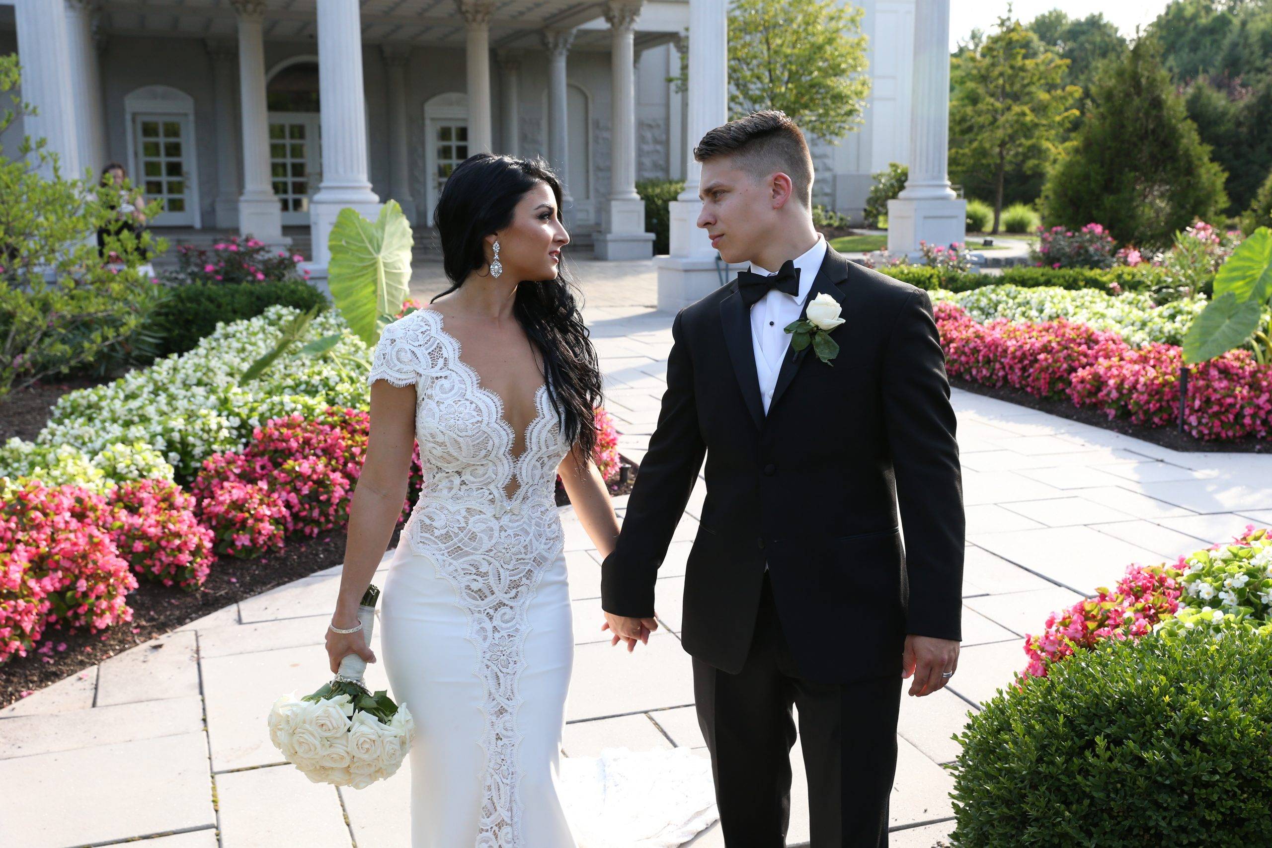 A bride and groom standing in front of a mansion.