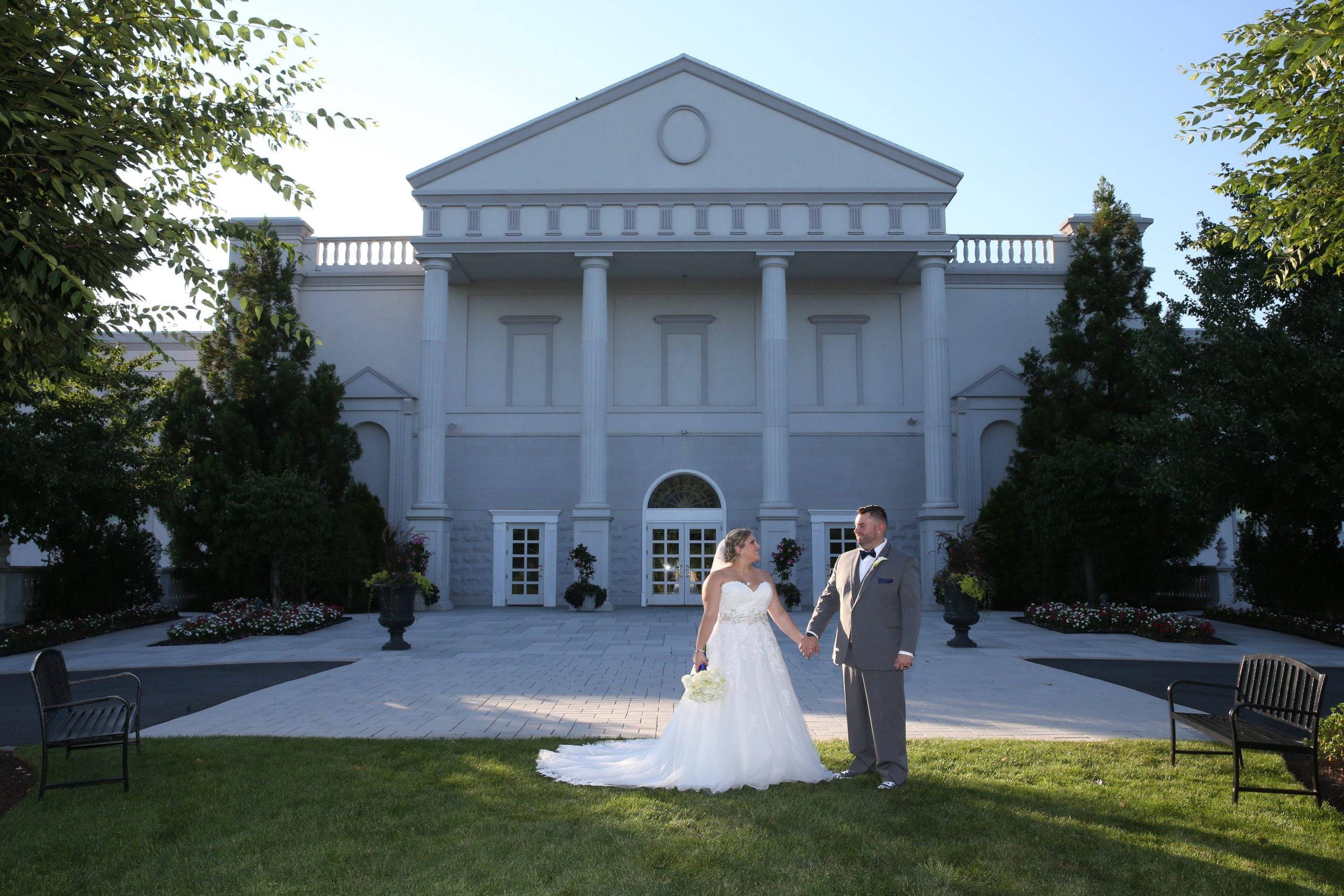 A bride and groom standing in front of a large white building.