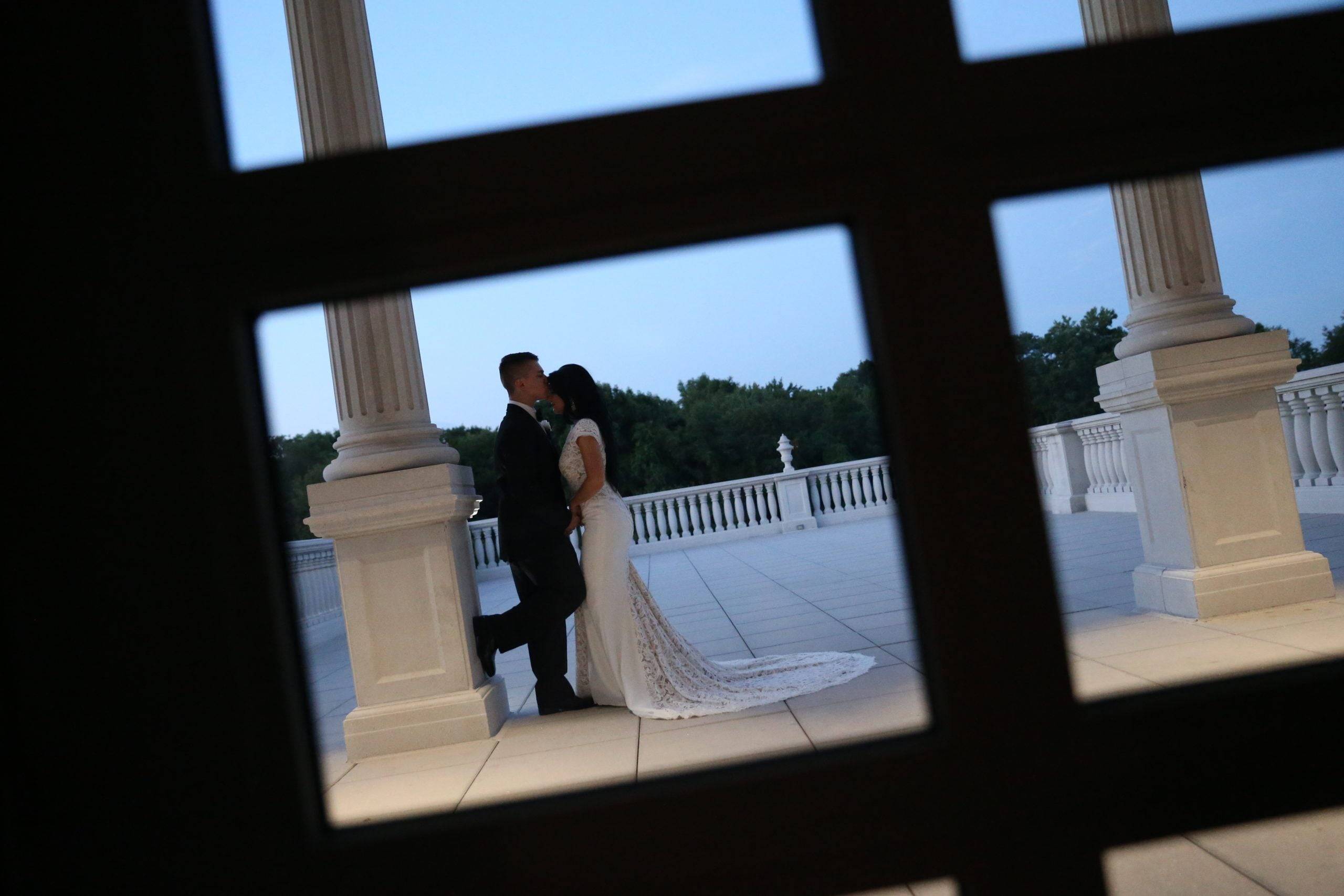 A bride and groom kissing through a window.