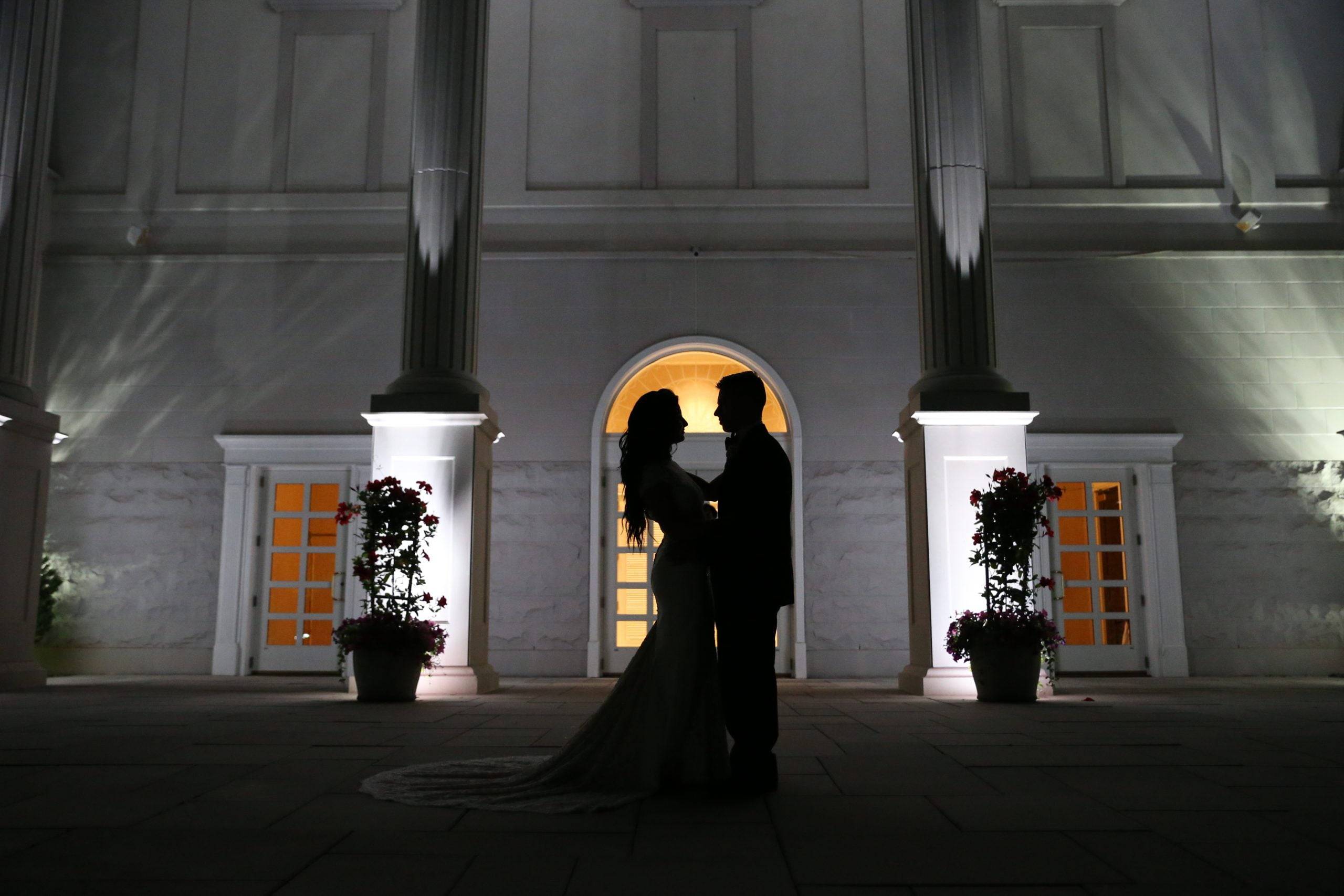 A bride and groom standing in front of a building at night.