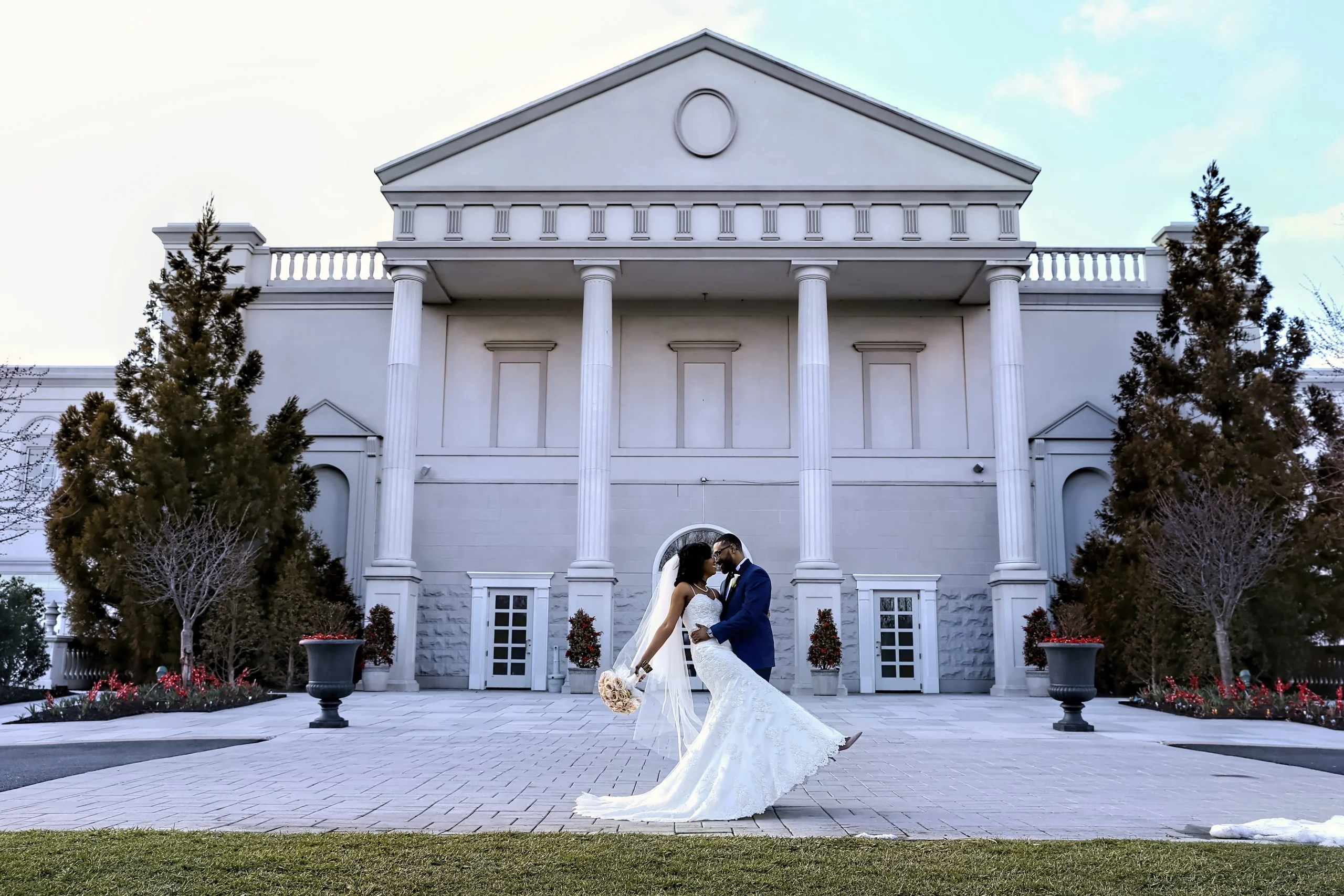 A bride and groom standing in front of a large white building.