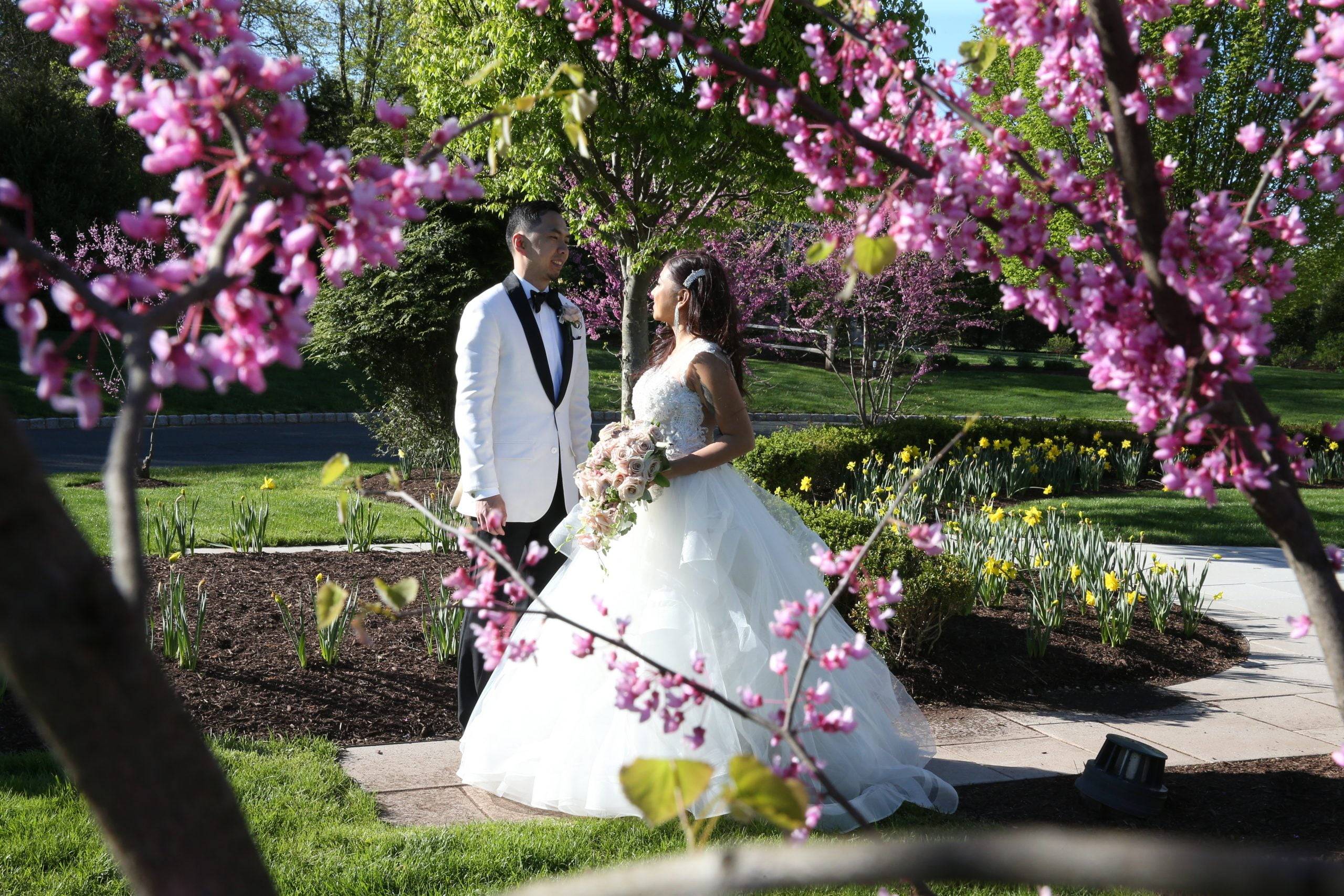 A bride and groom standing in front of a pink flowering tree.