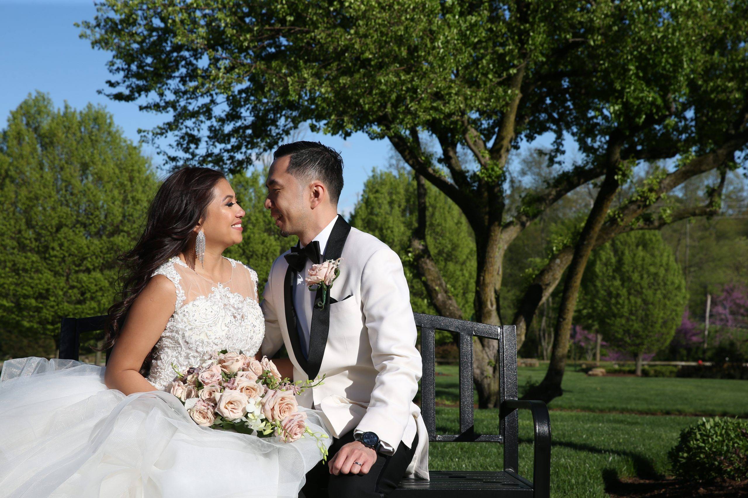 A bride and groom sitting on a bench in a park.