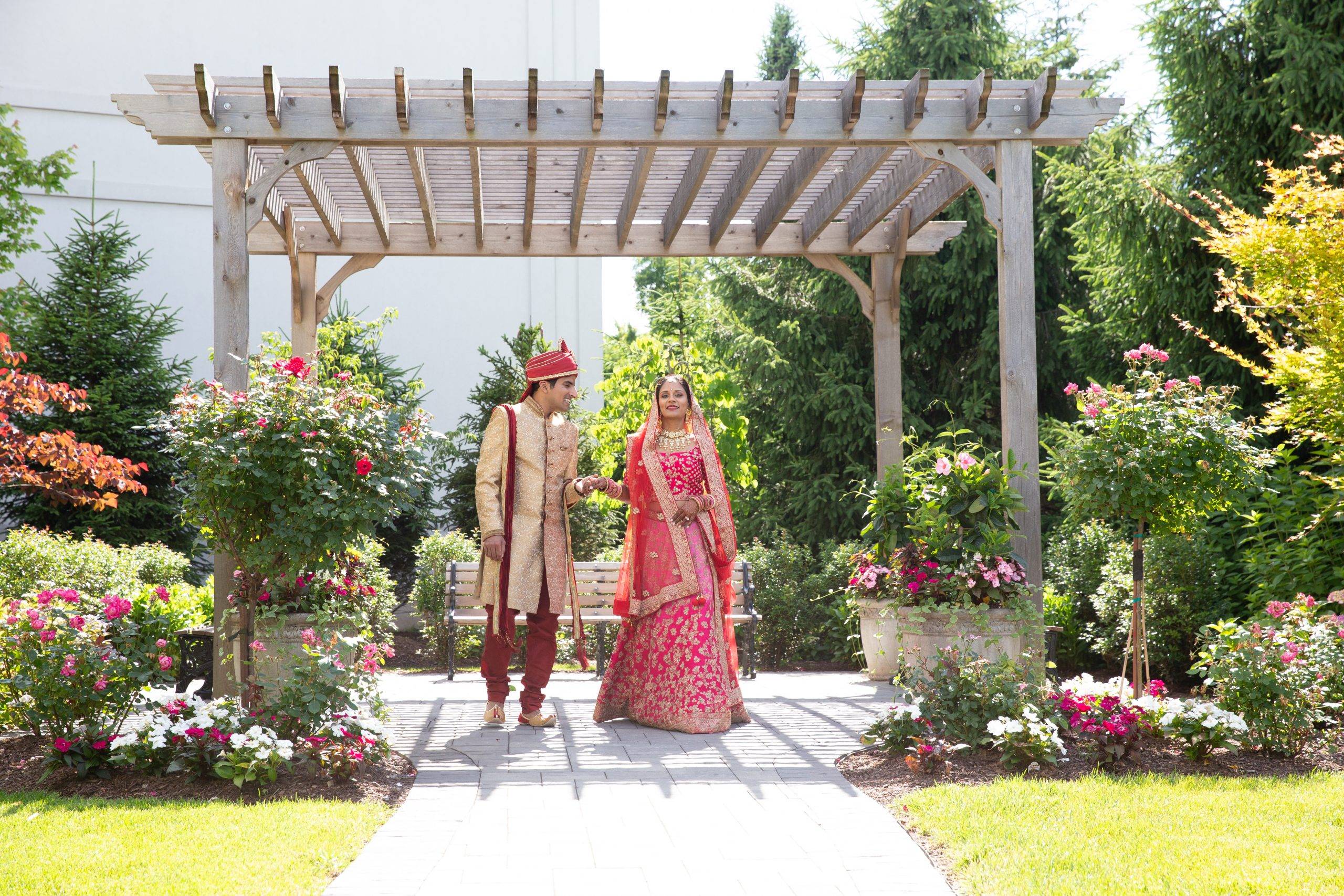 A bride and groom standing under a gazebo in a garden.