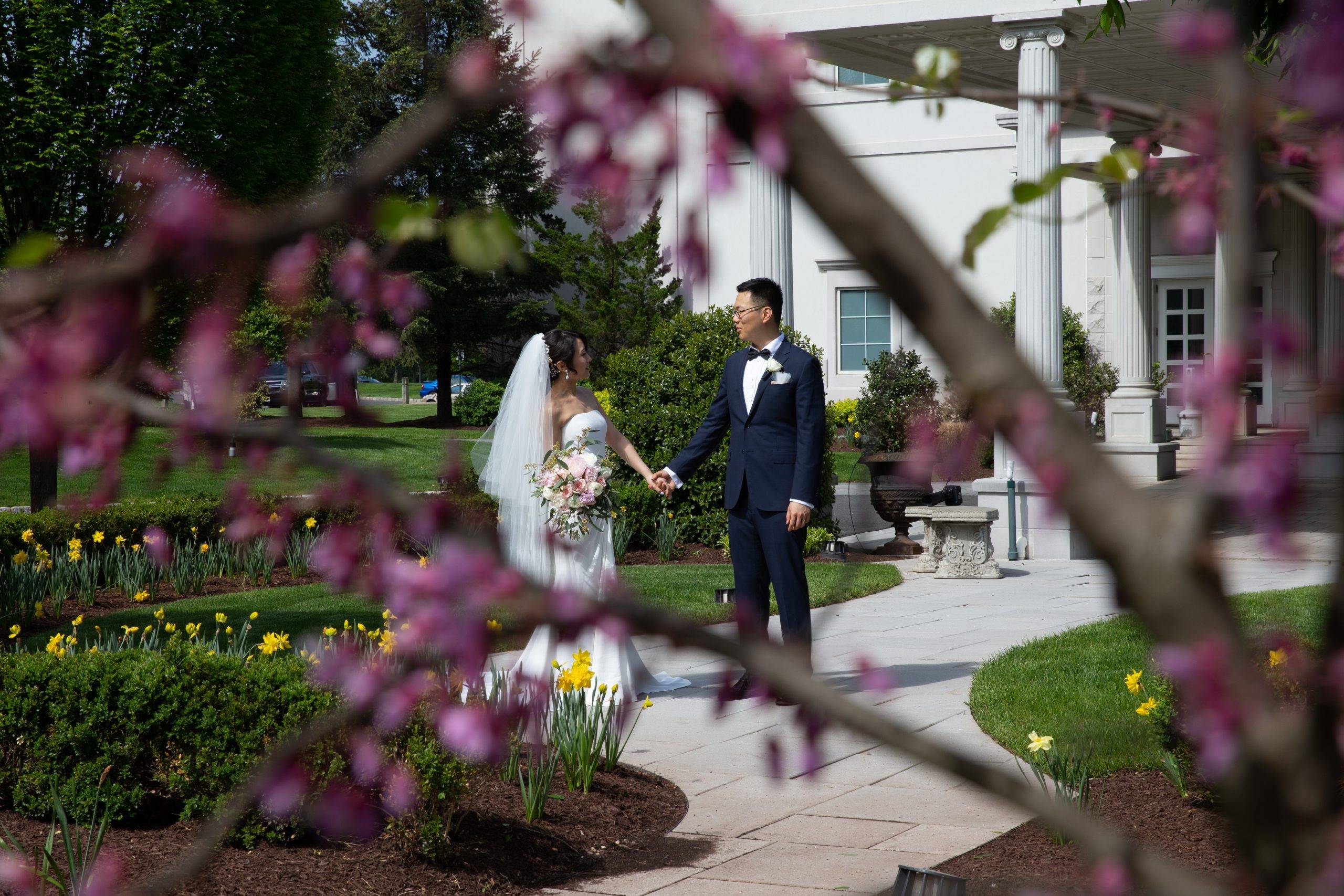 A bride and groom walking down a path in front of a house.