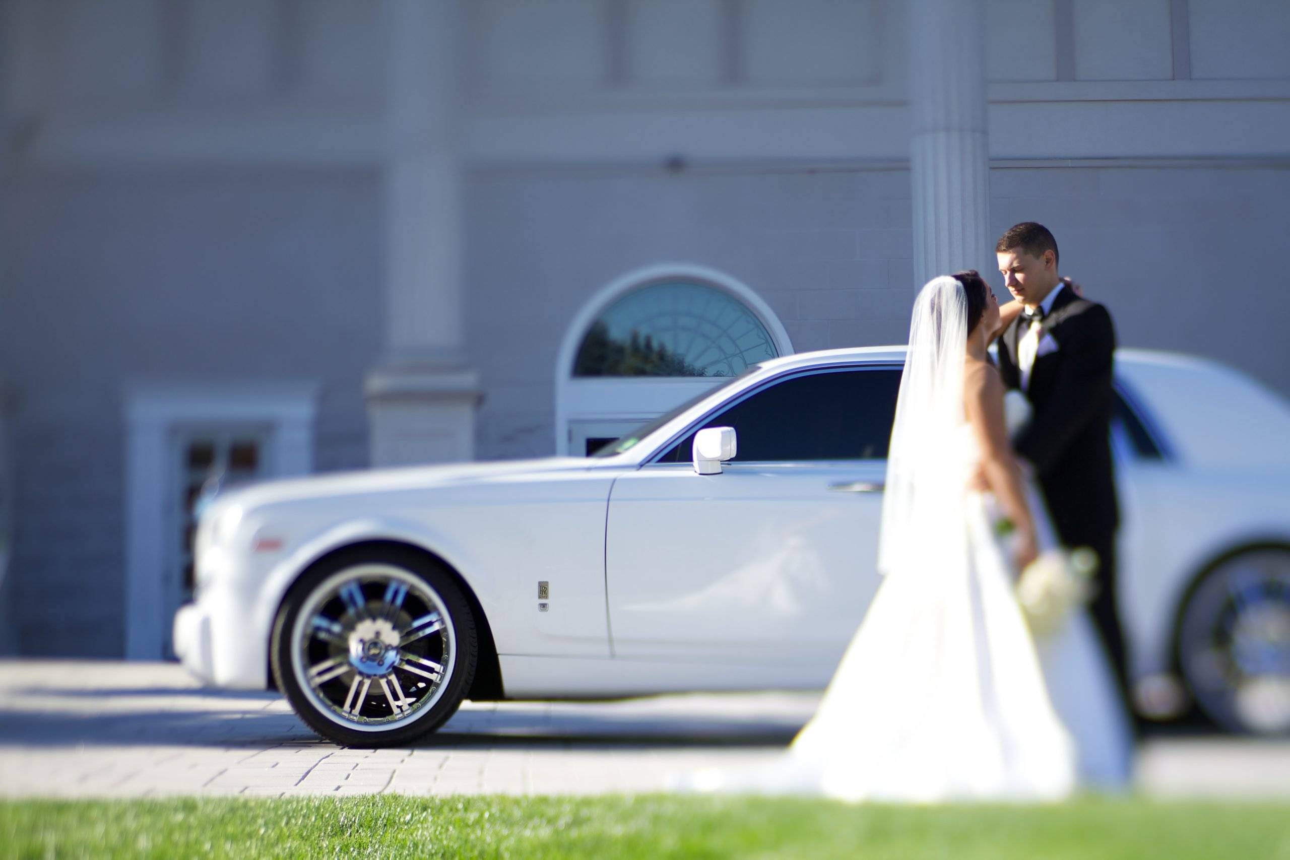 A bride and groom standing next to a white rolls royce car.