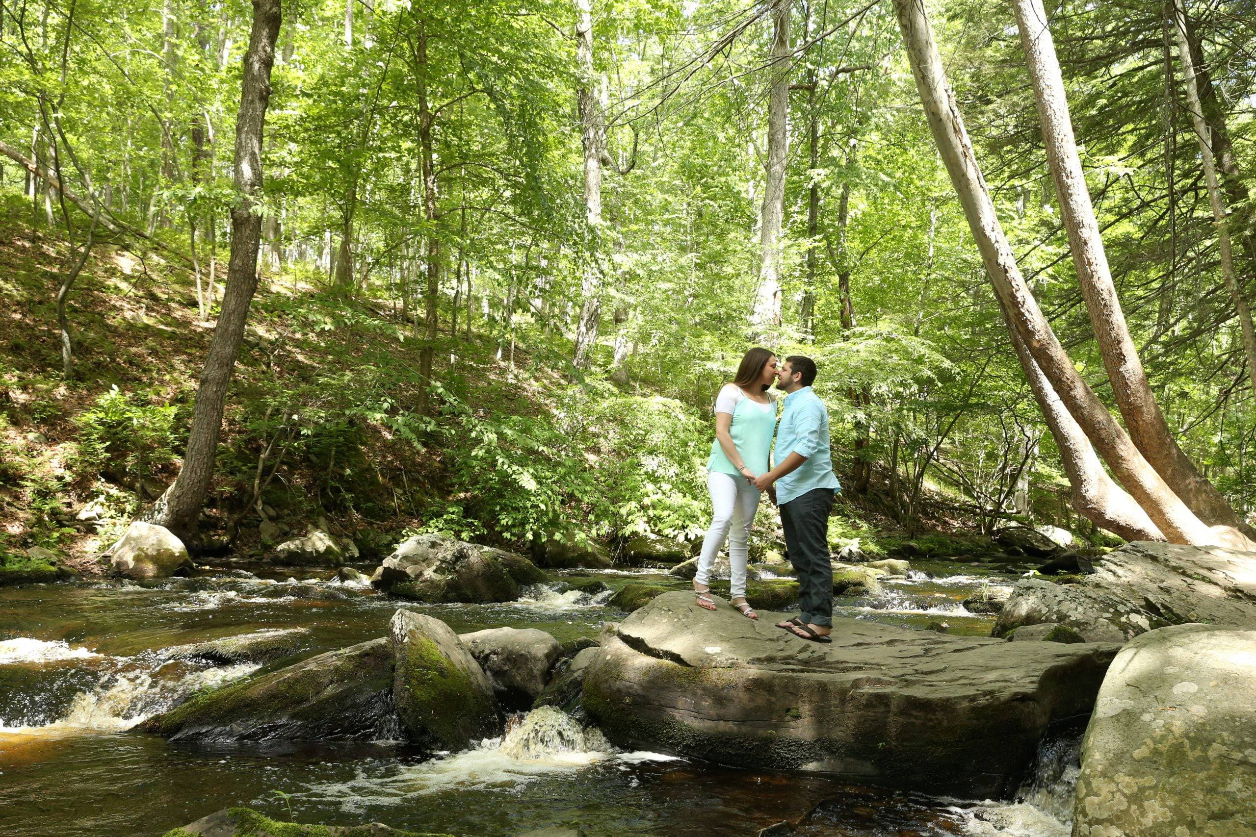 A couple standing on rocks near a stream in the woods.