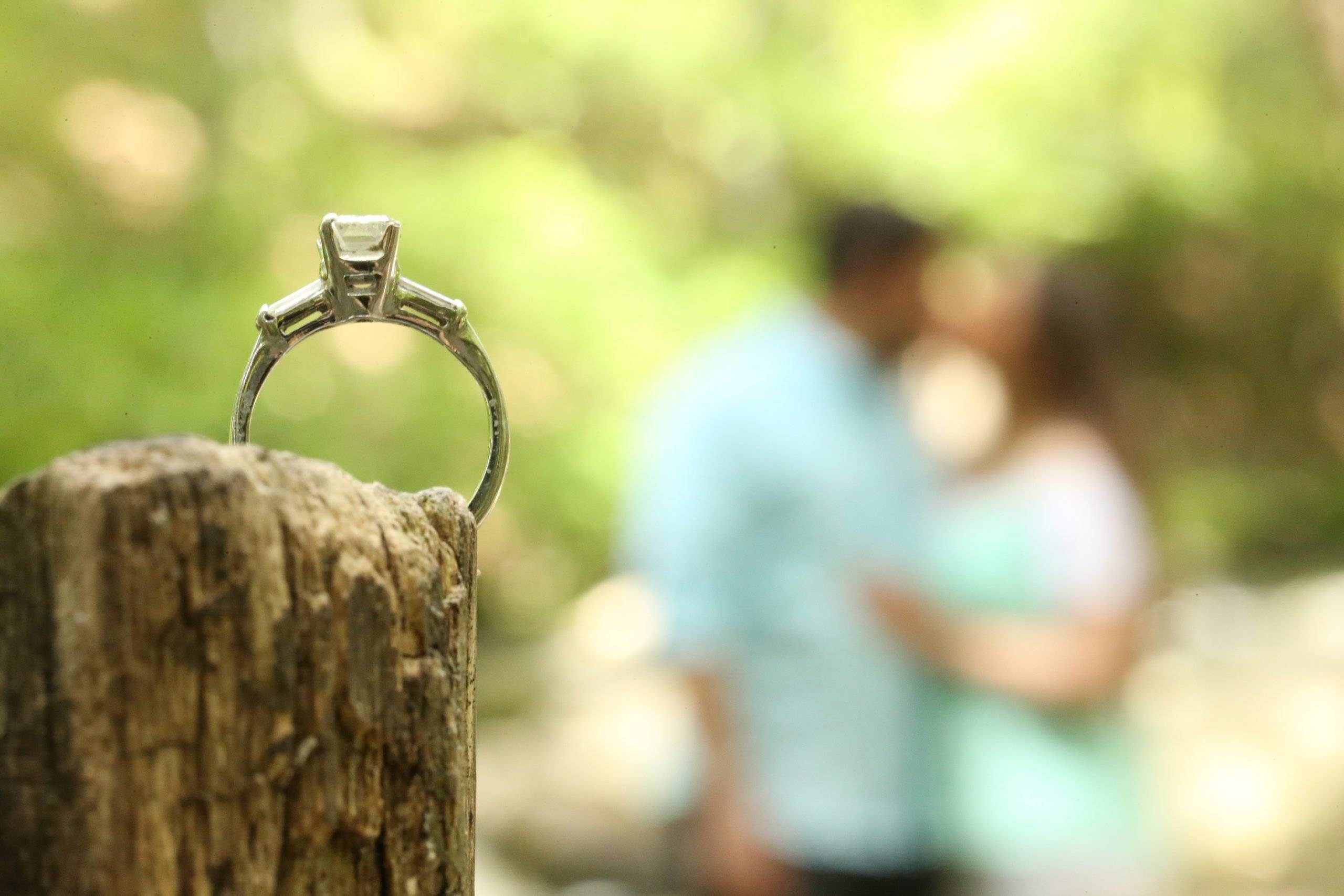 An engagement ring sits on top of a wooden post.