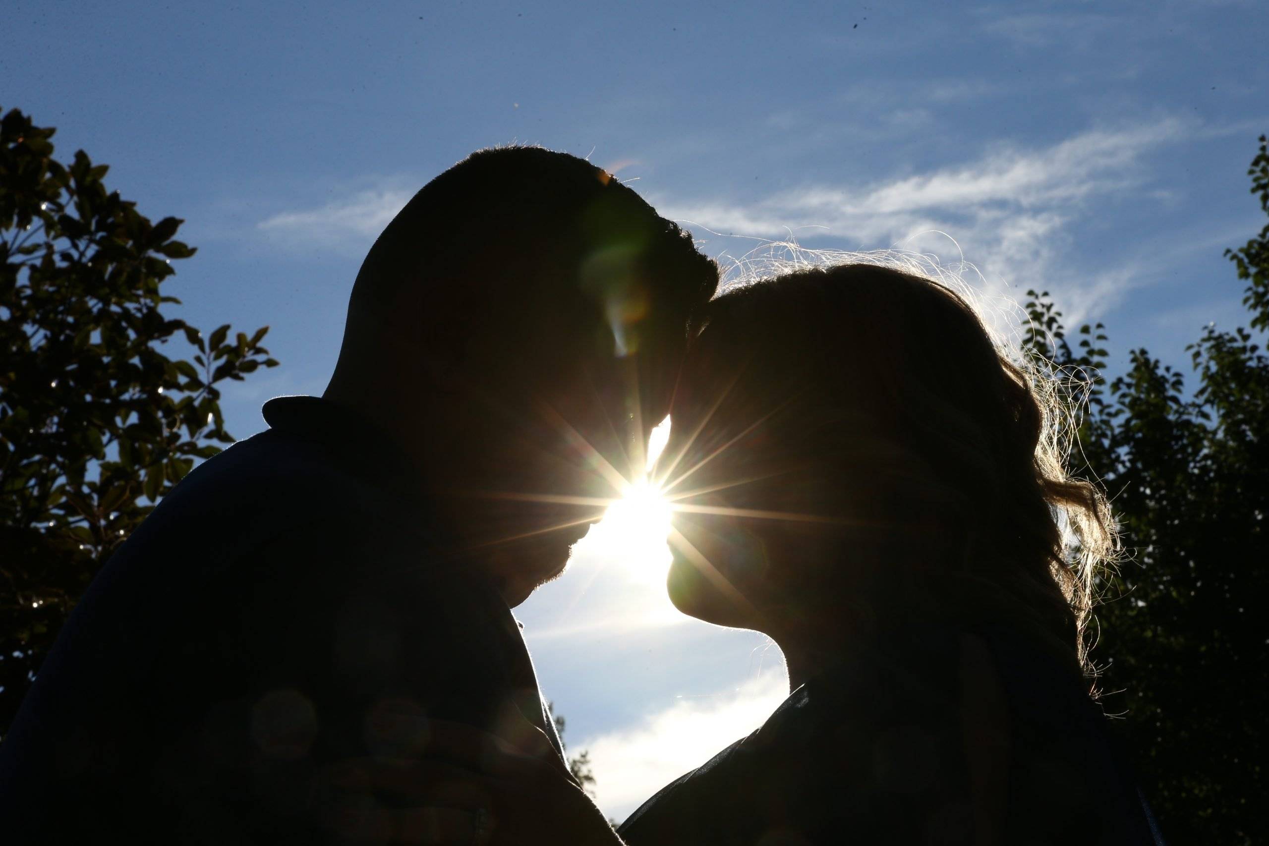 A silhouette of a couple kissing in front of the sun.