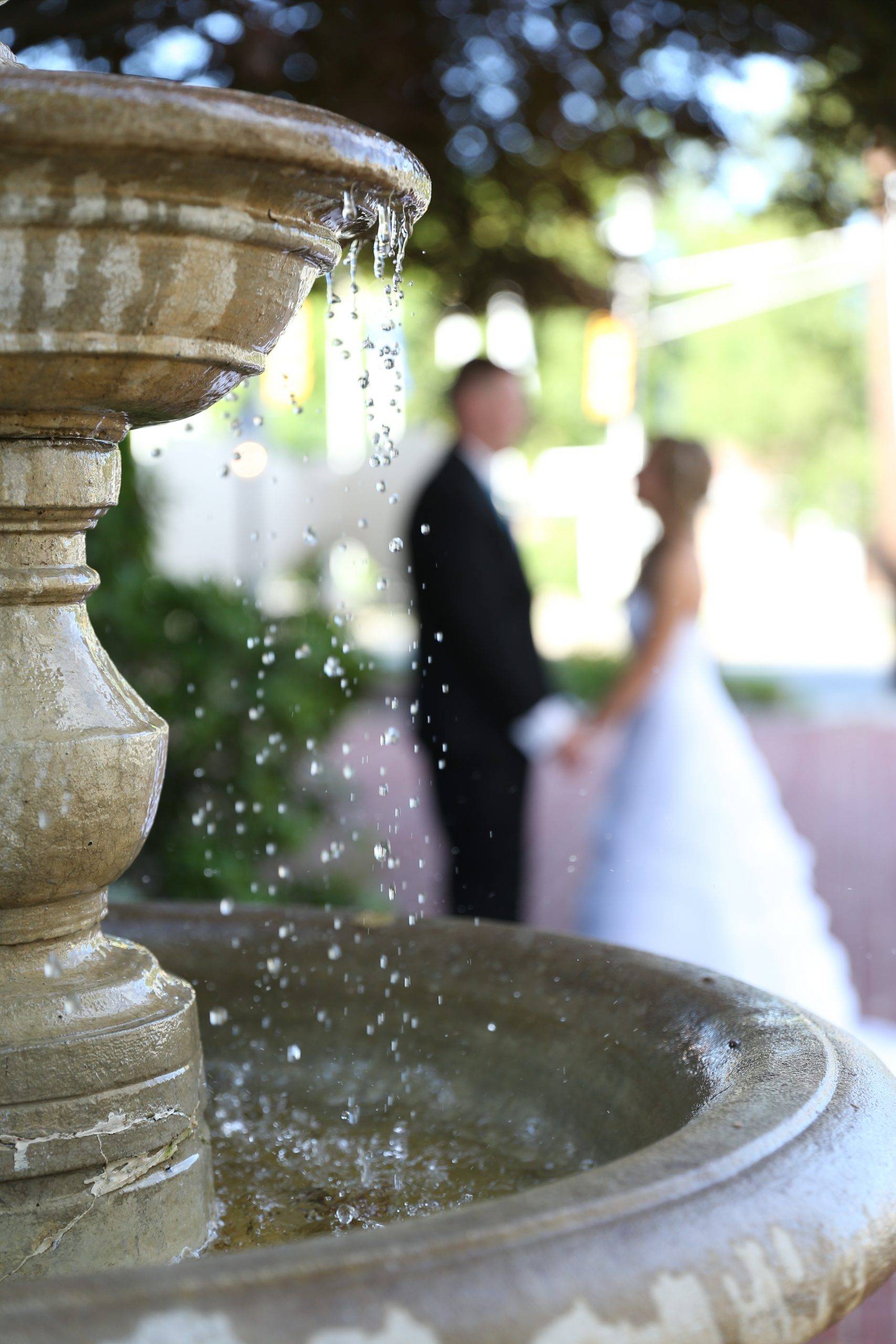 A bride and groom standing in front of a fountain.