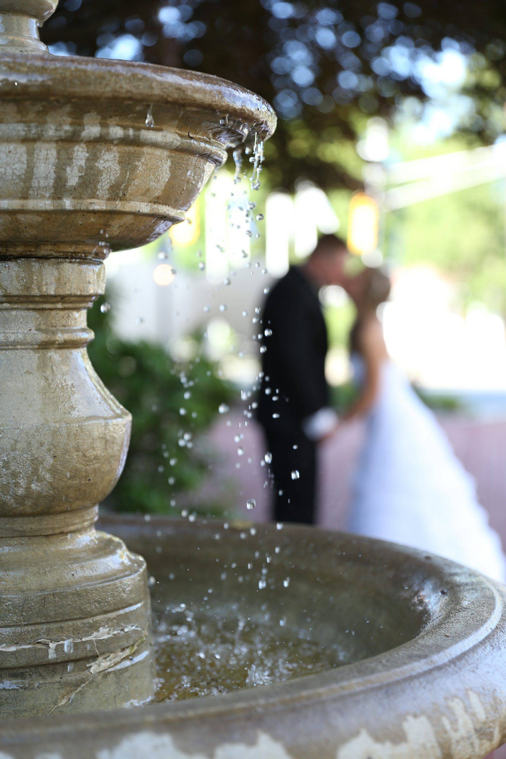 A bride and groom kissing in front of a water fountain.