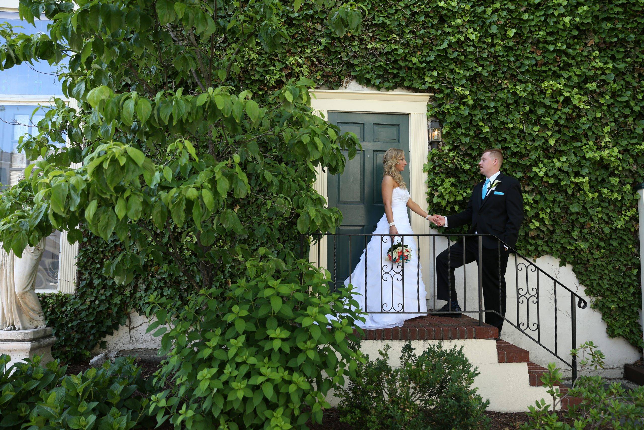 A bride and groom standing on the steps of a house with ivy.