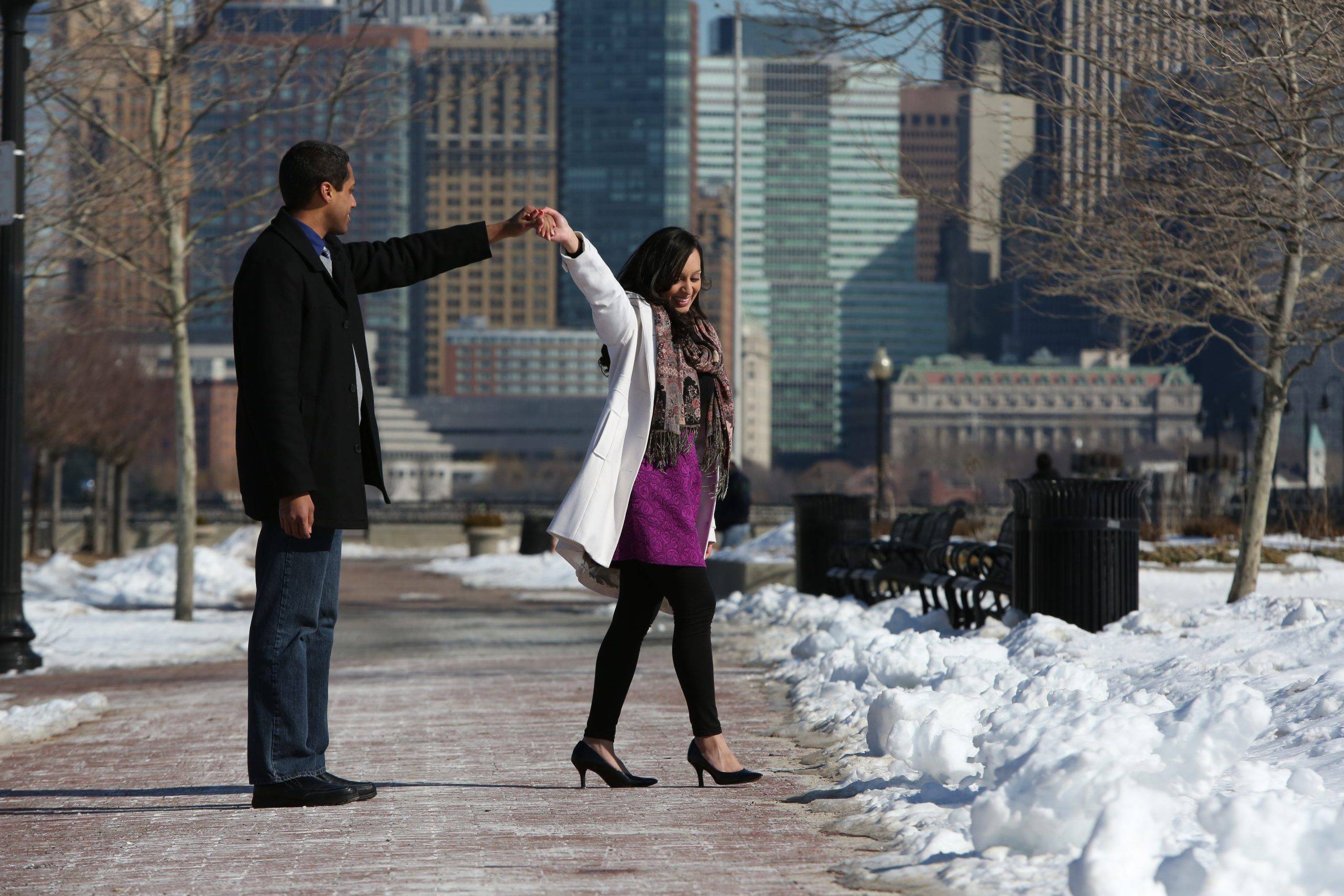 A man and woman walking in the snow with a city in the background.