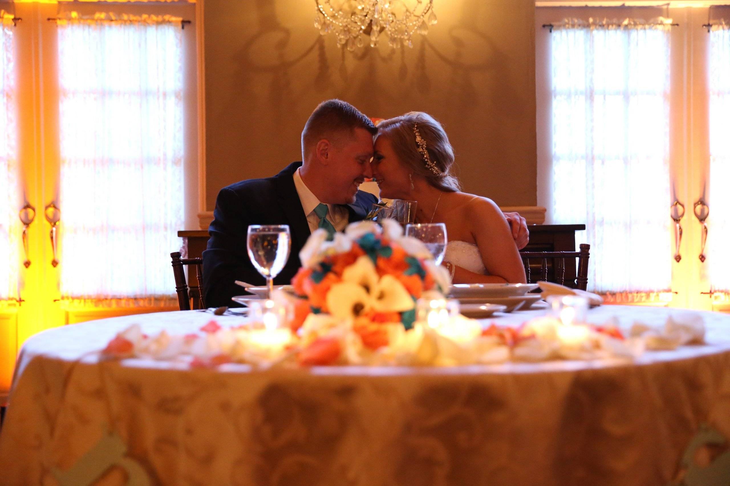 A bride and groom kissing at their wedding table.