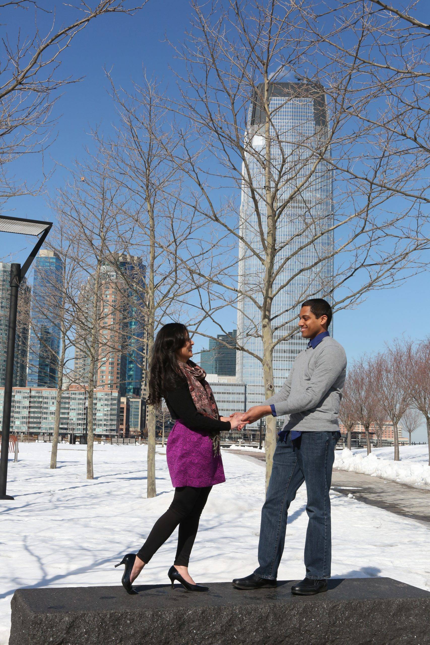 A man and woman standing in the snow in front of a skyscraper.
