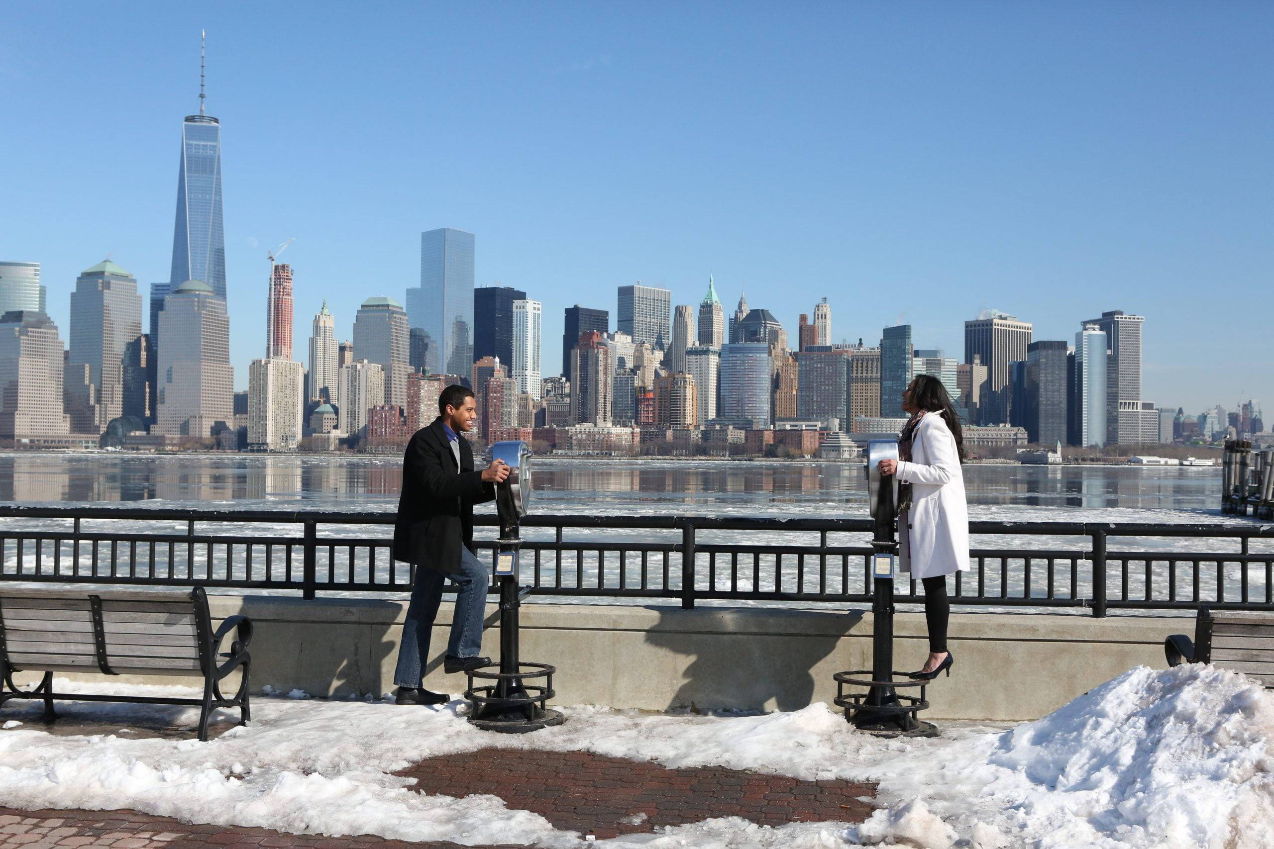 Two people standing on a bench in front of the manhattan skyline.