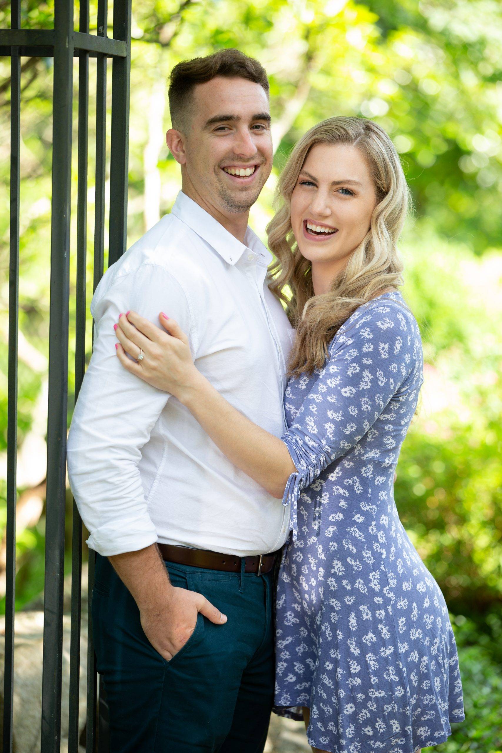 A couple posing in front of a fence in a park.