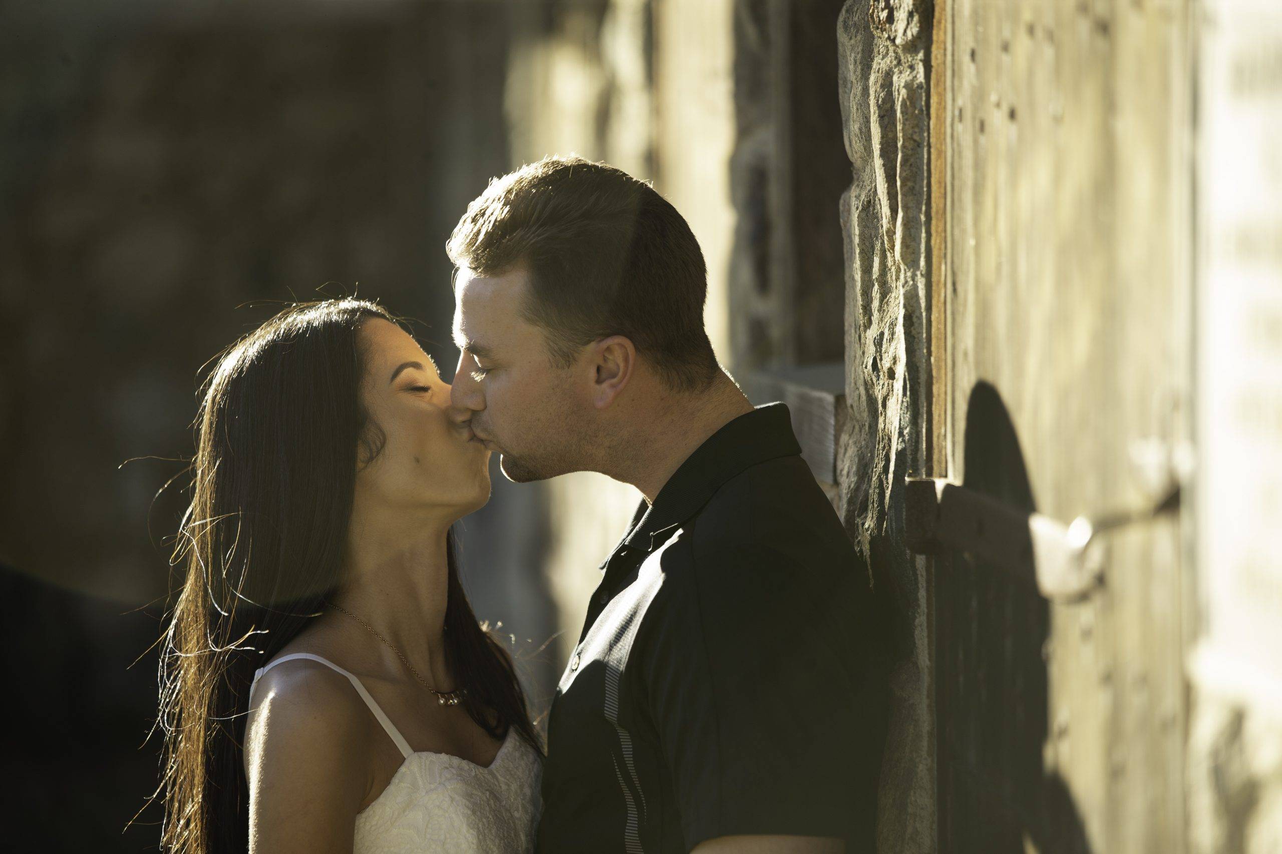A couple kissing in front of a stone wall.