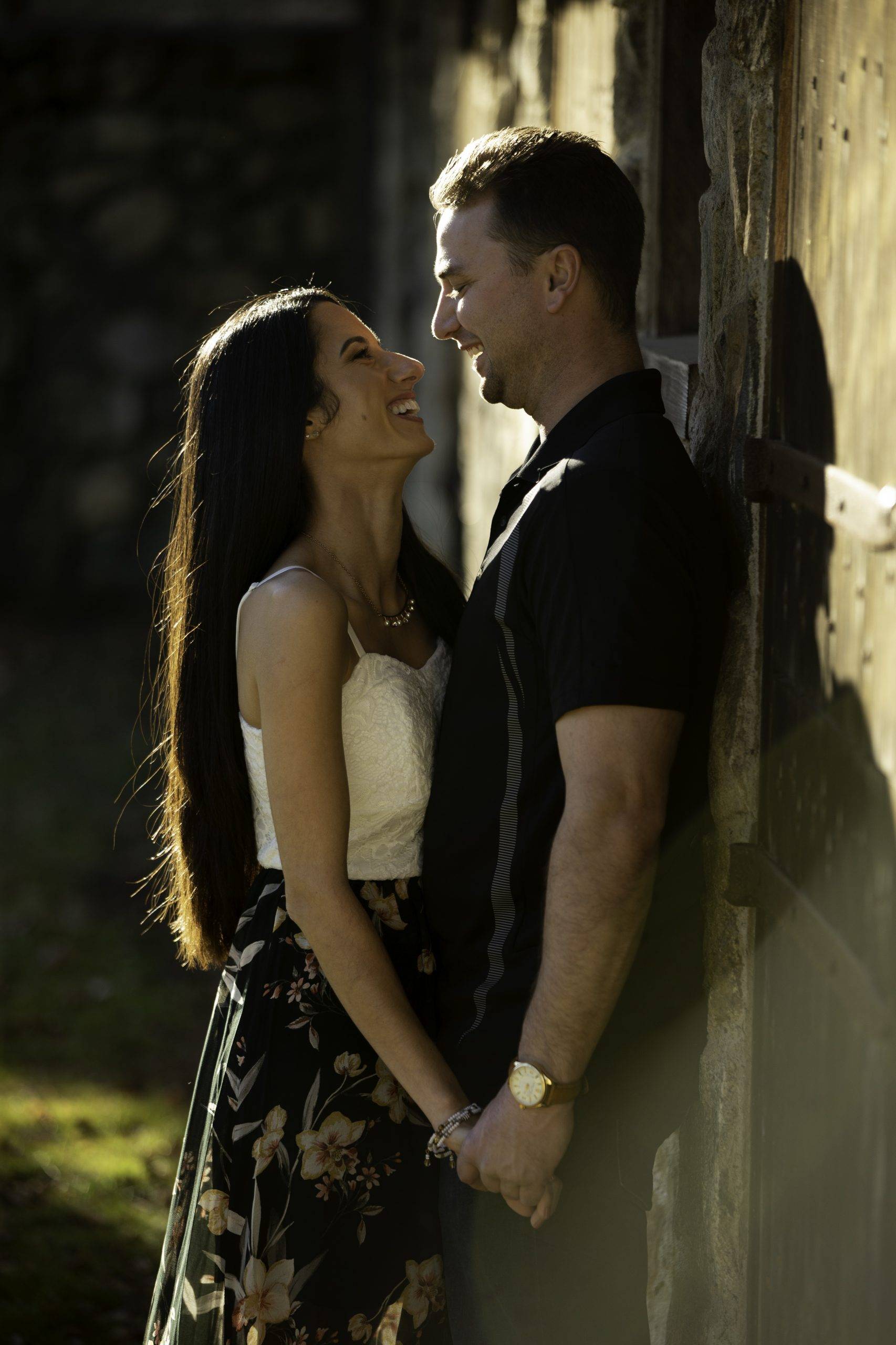 A couple is leaning against a stone wall during their engagement session.