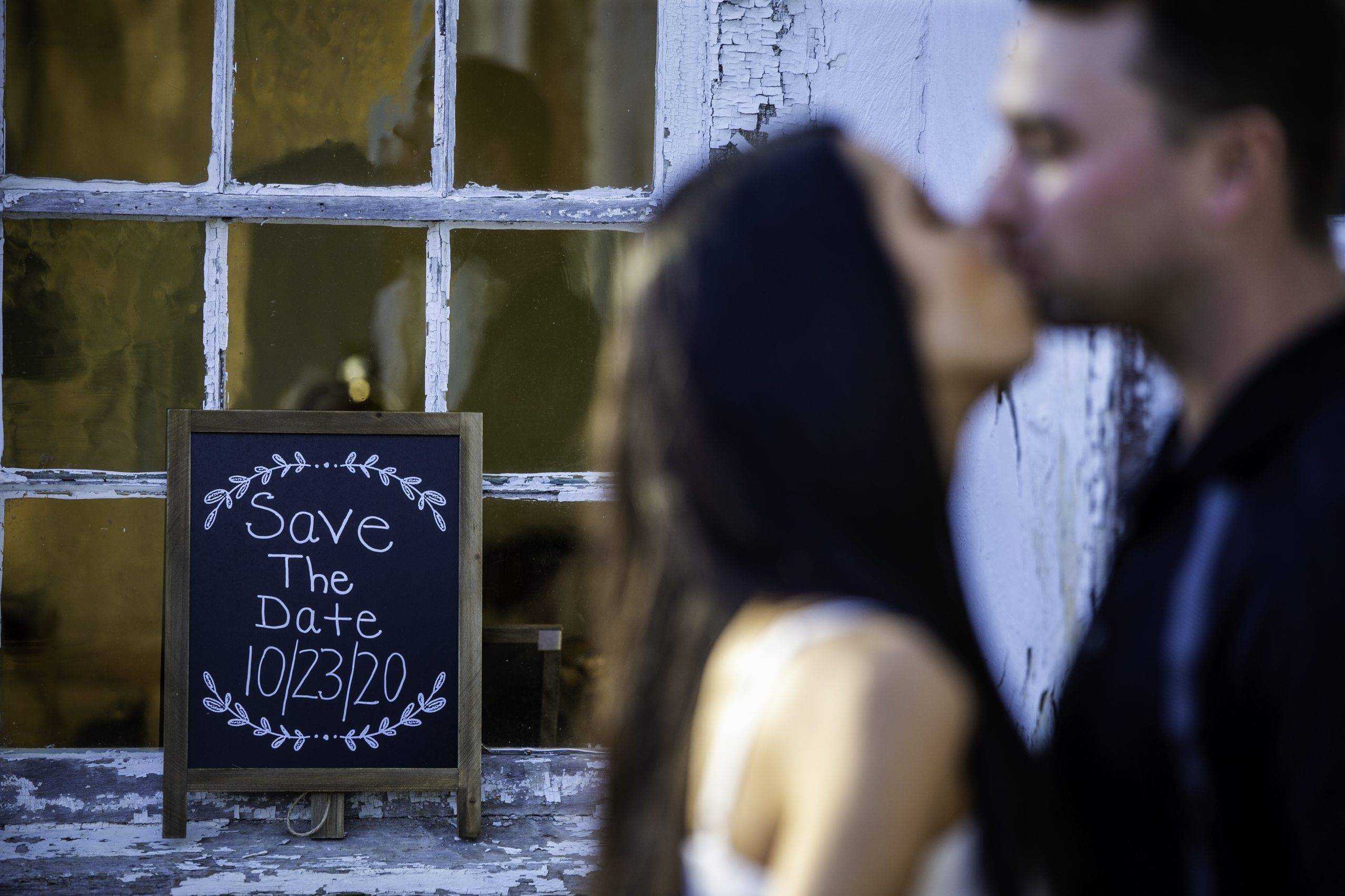 A couple kisses in front of a sign that says save the date.