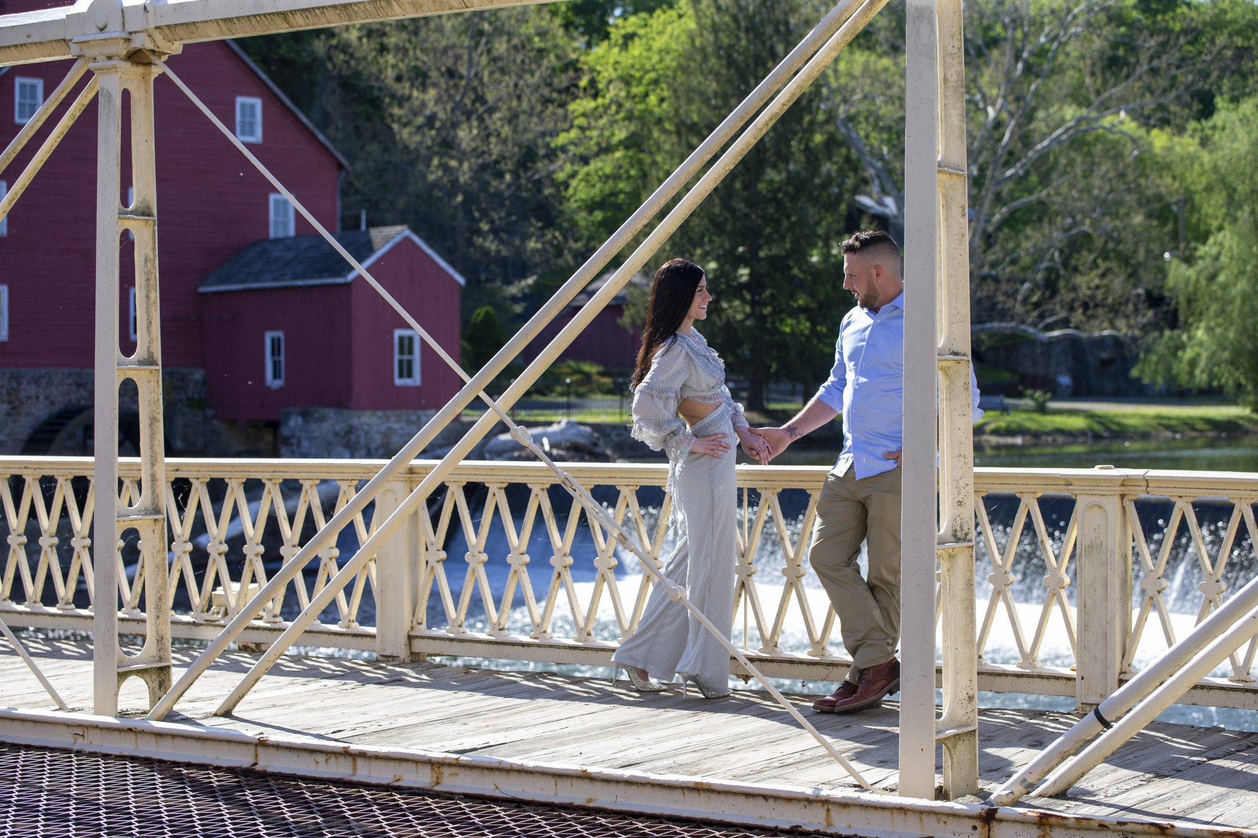 An engaged couple standing on a bridge over a river.