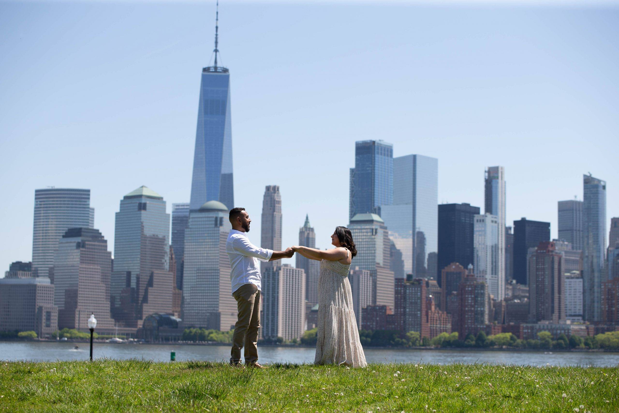 A man and woman standing in a field with a city skyline in the background.