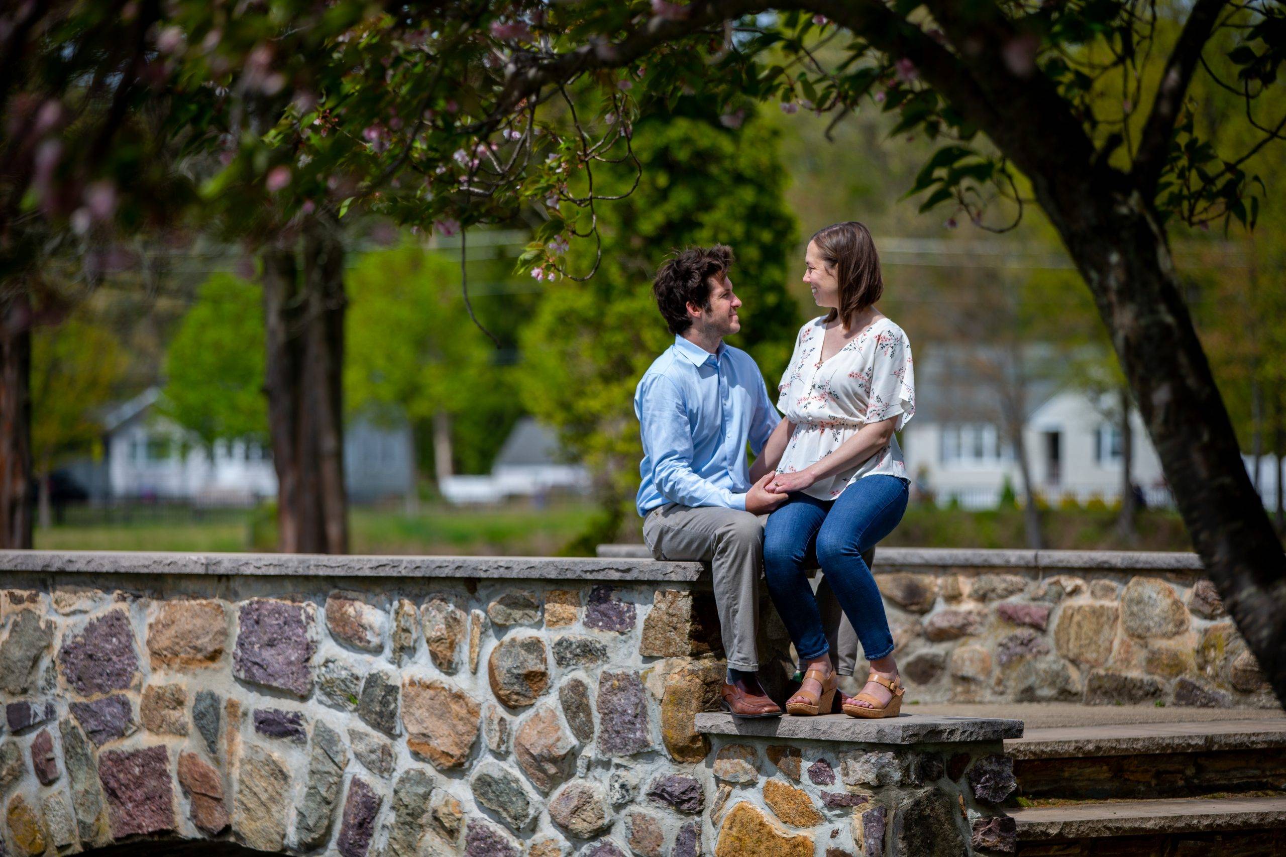 An engaged couple sitting on a stone wall.