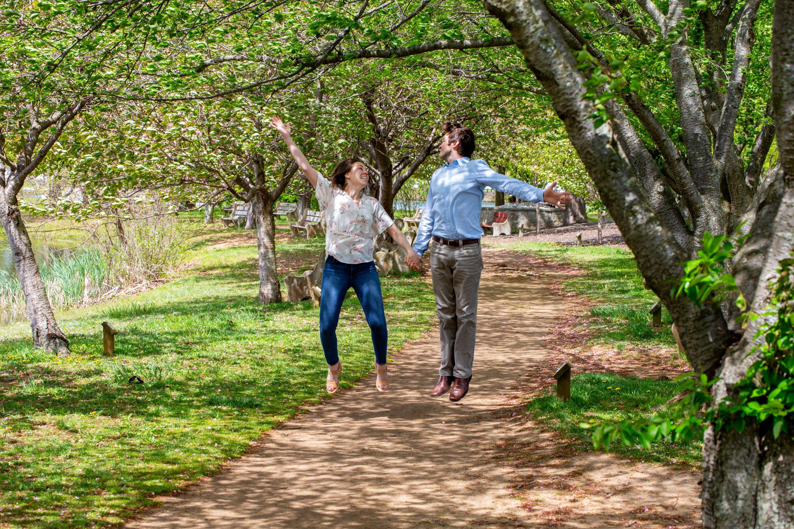 A couple jumping in the air on a path in a park.