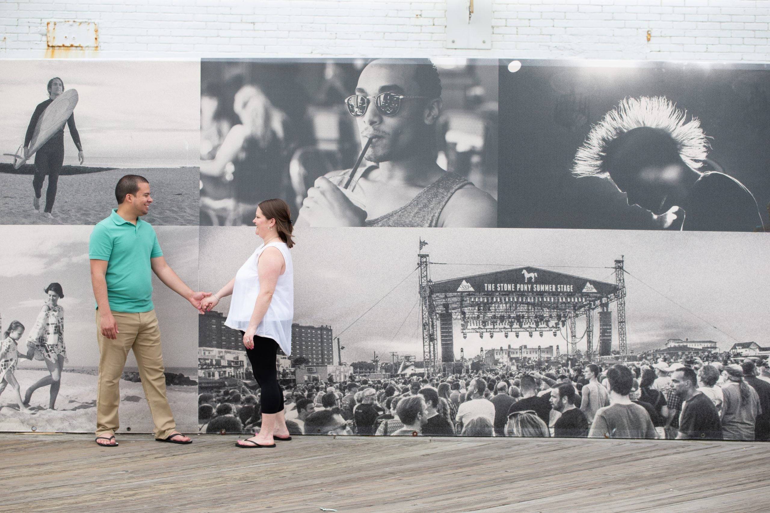 A couple holding hands in front of a wall of photos.