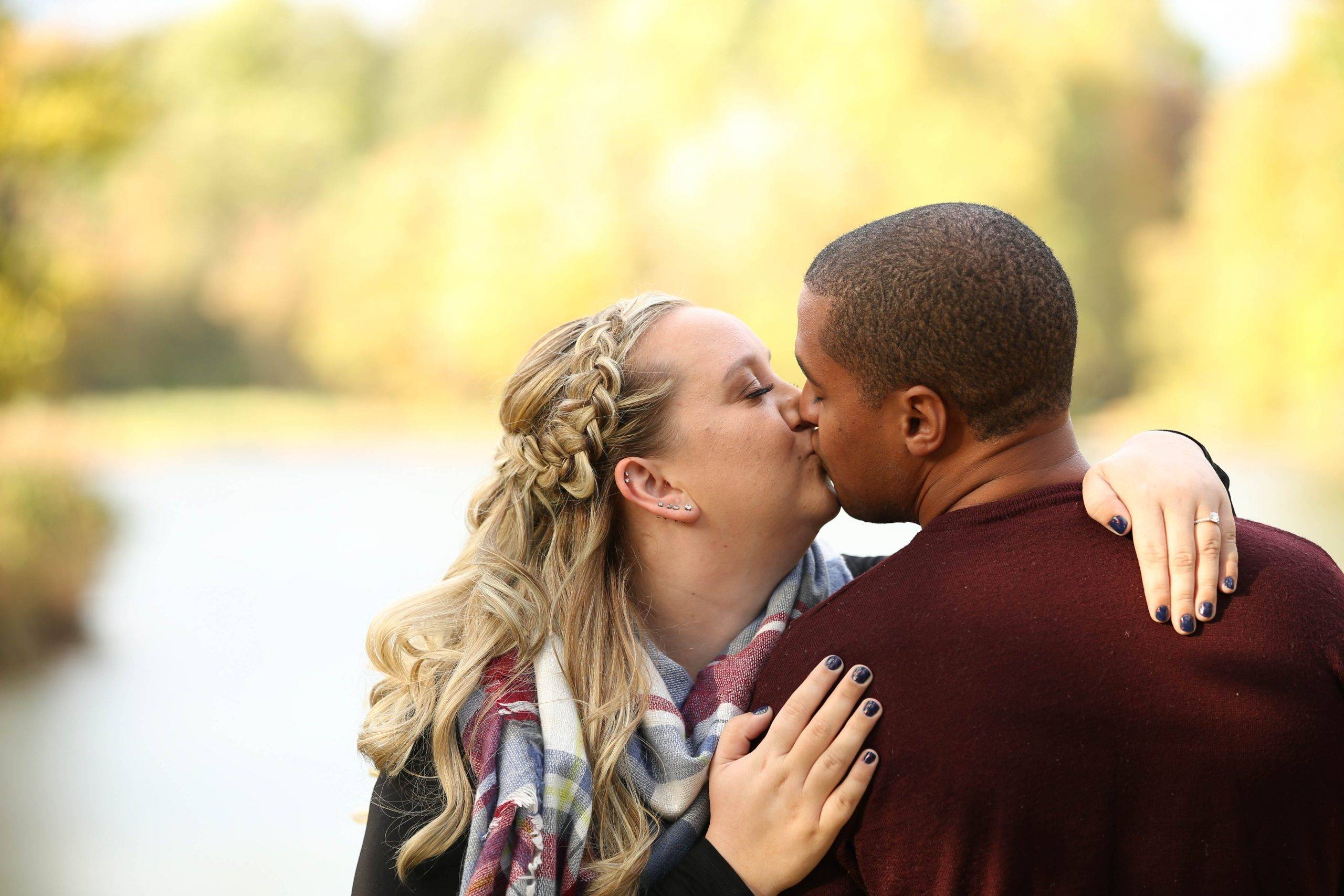 A man and woman kissing in front of a lake.