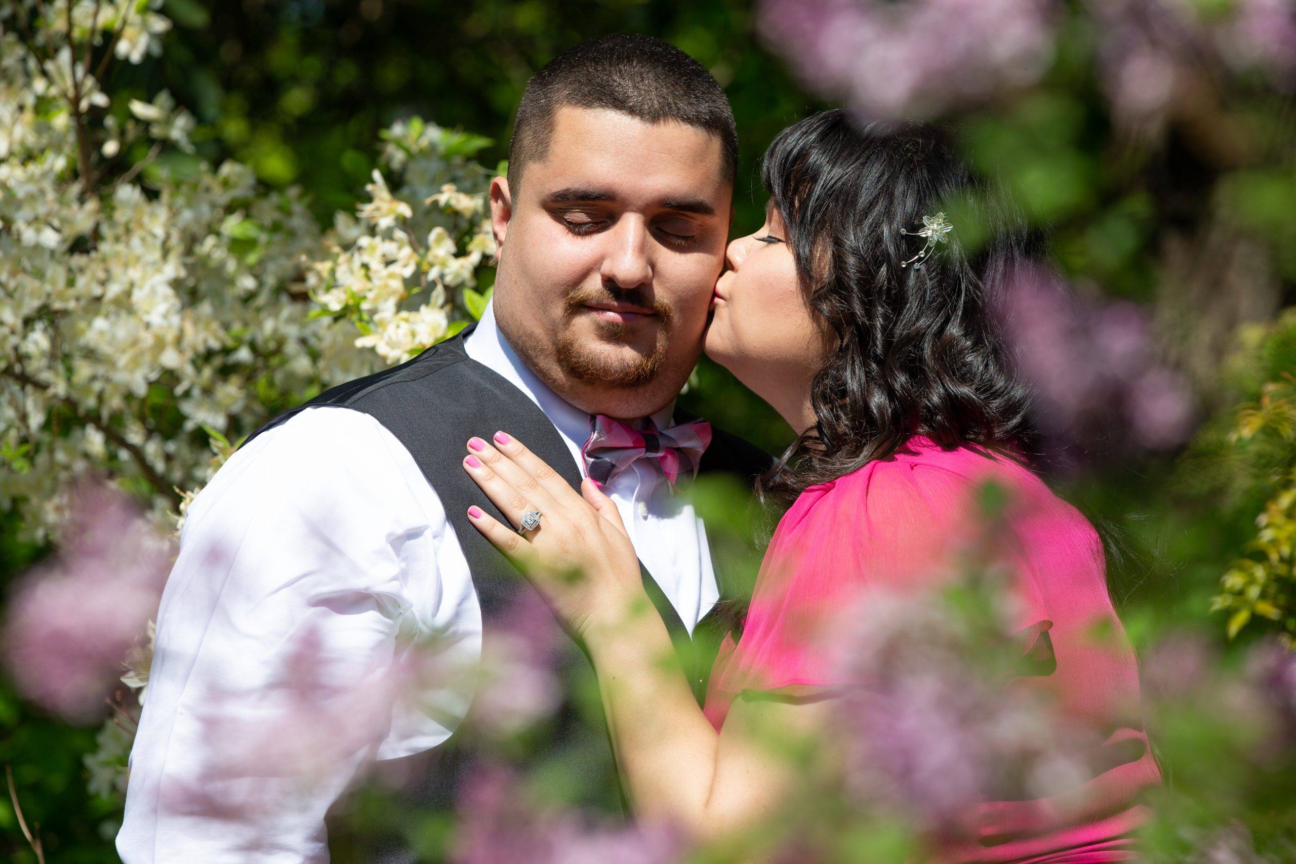 A man and woman kissing in front of lilacs.