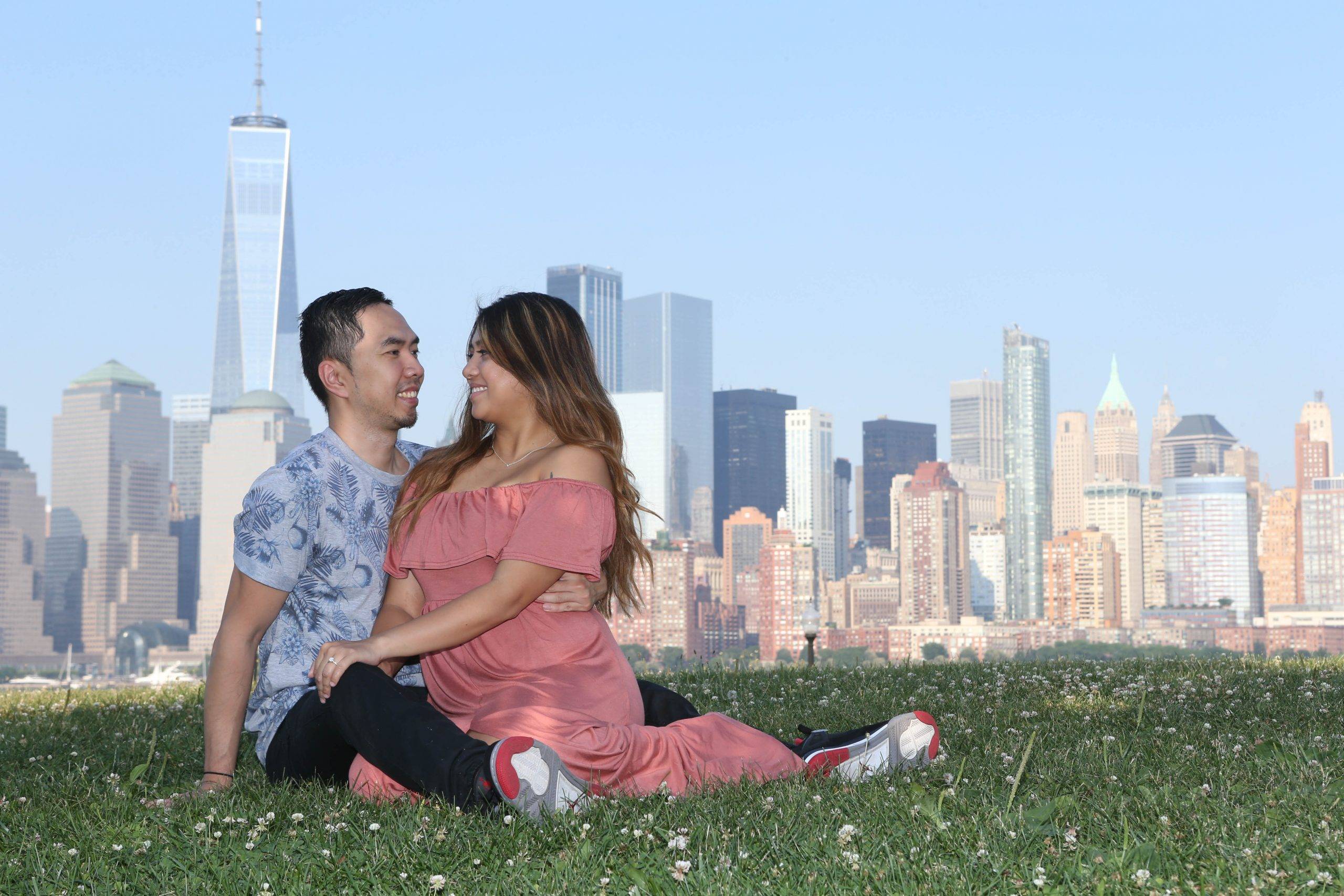 A couple sits on the grass in front of the manhattan skyline.