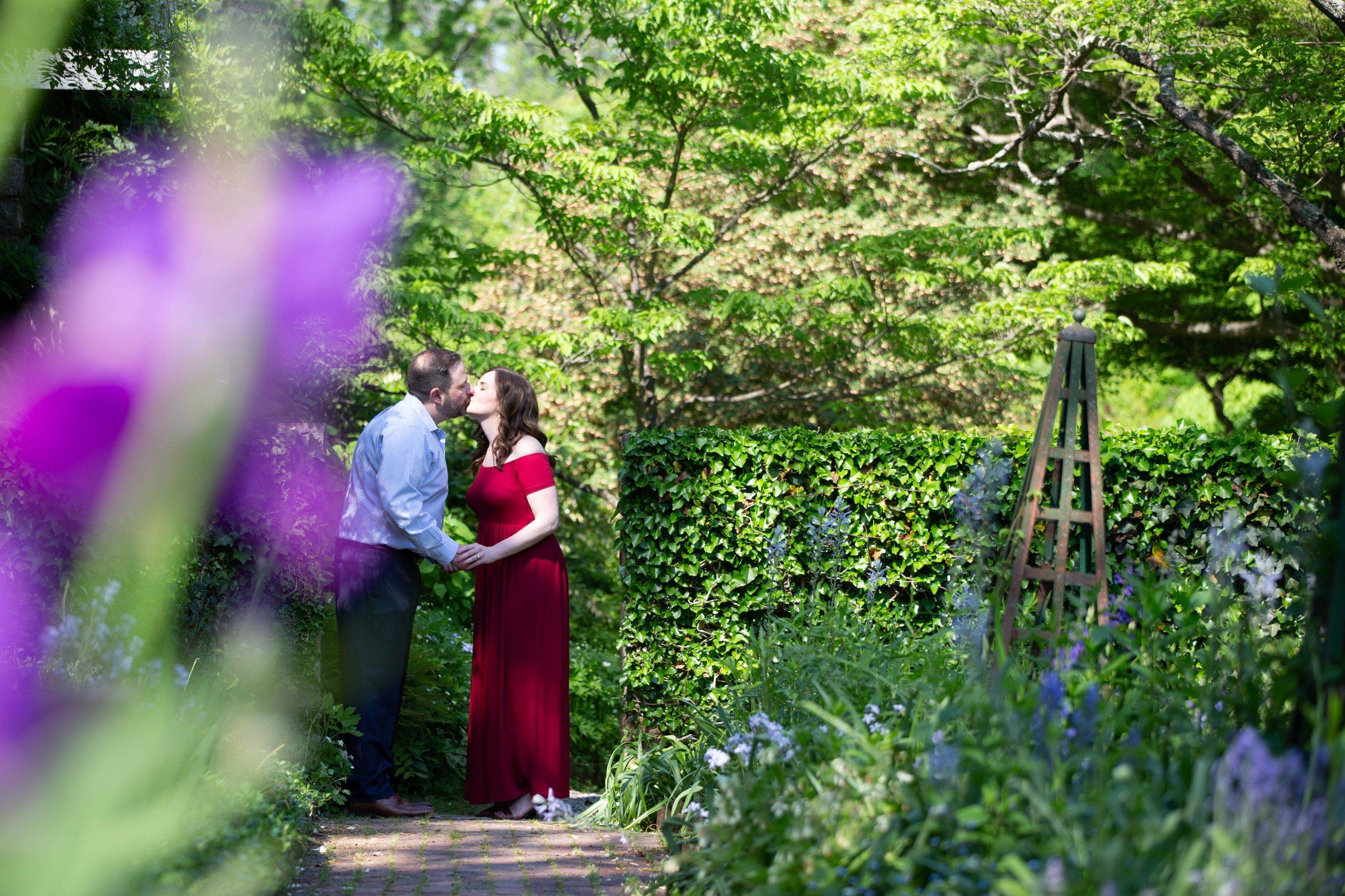 An engaged couple kissing in a garden.