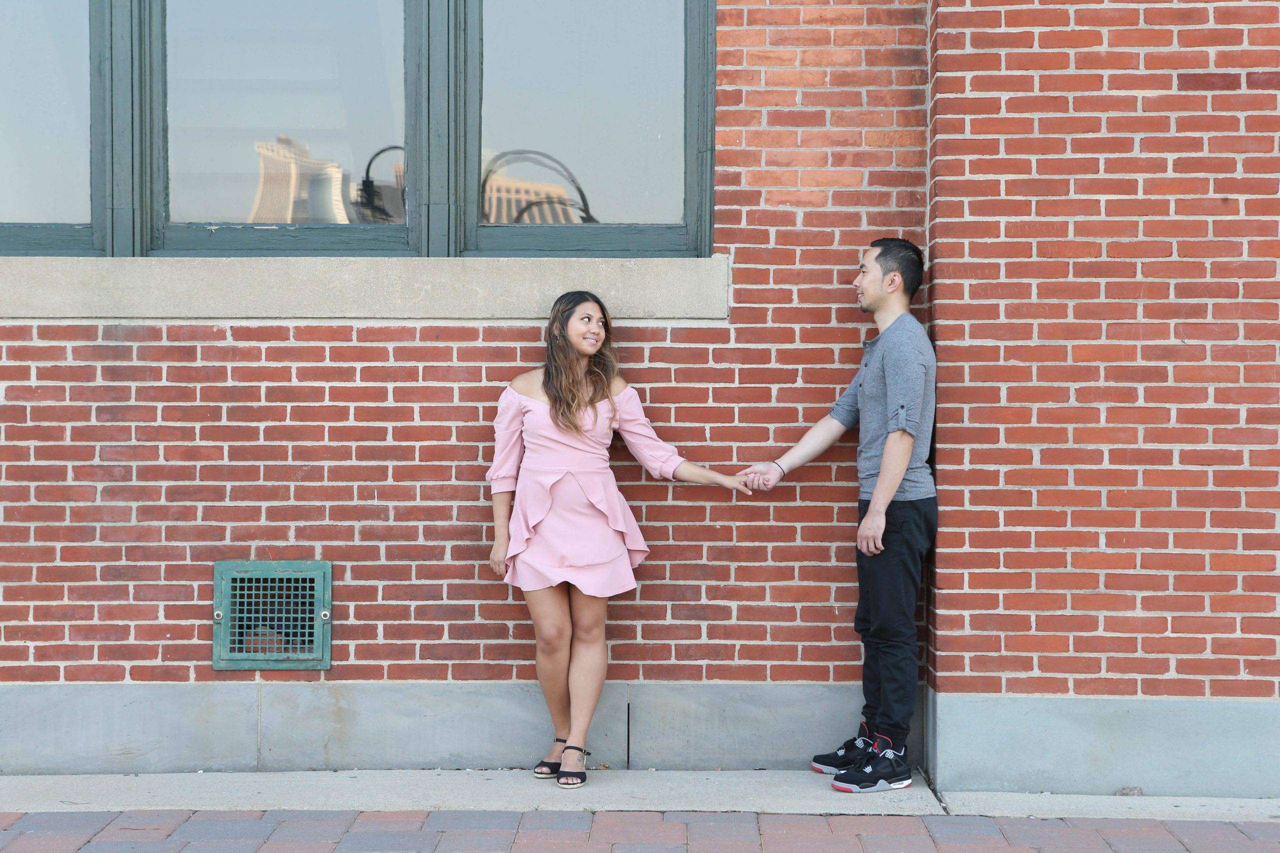 A couple holding hands in front of a brick wall.