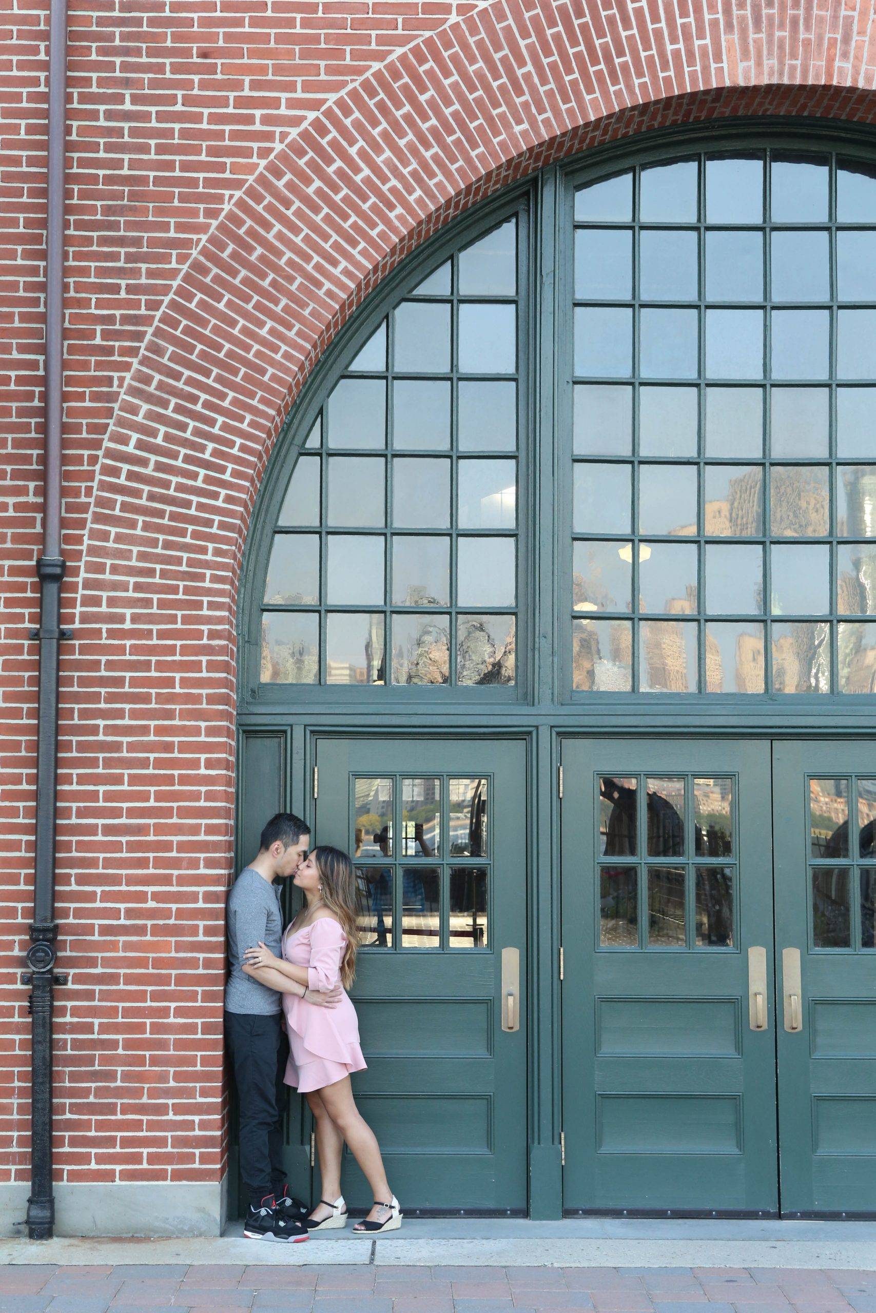A couple kisses in front of a red brick building.