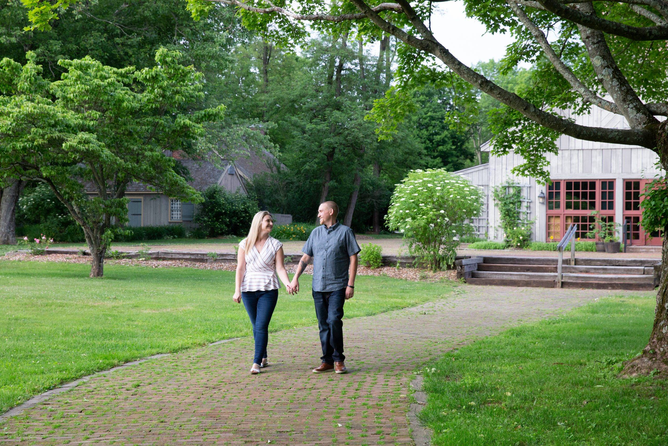 A couple walking down a brick walkway in a park.