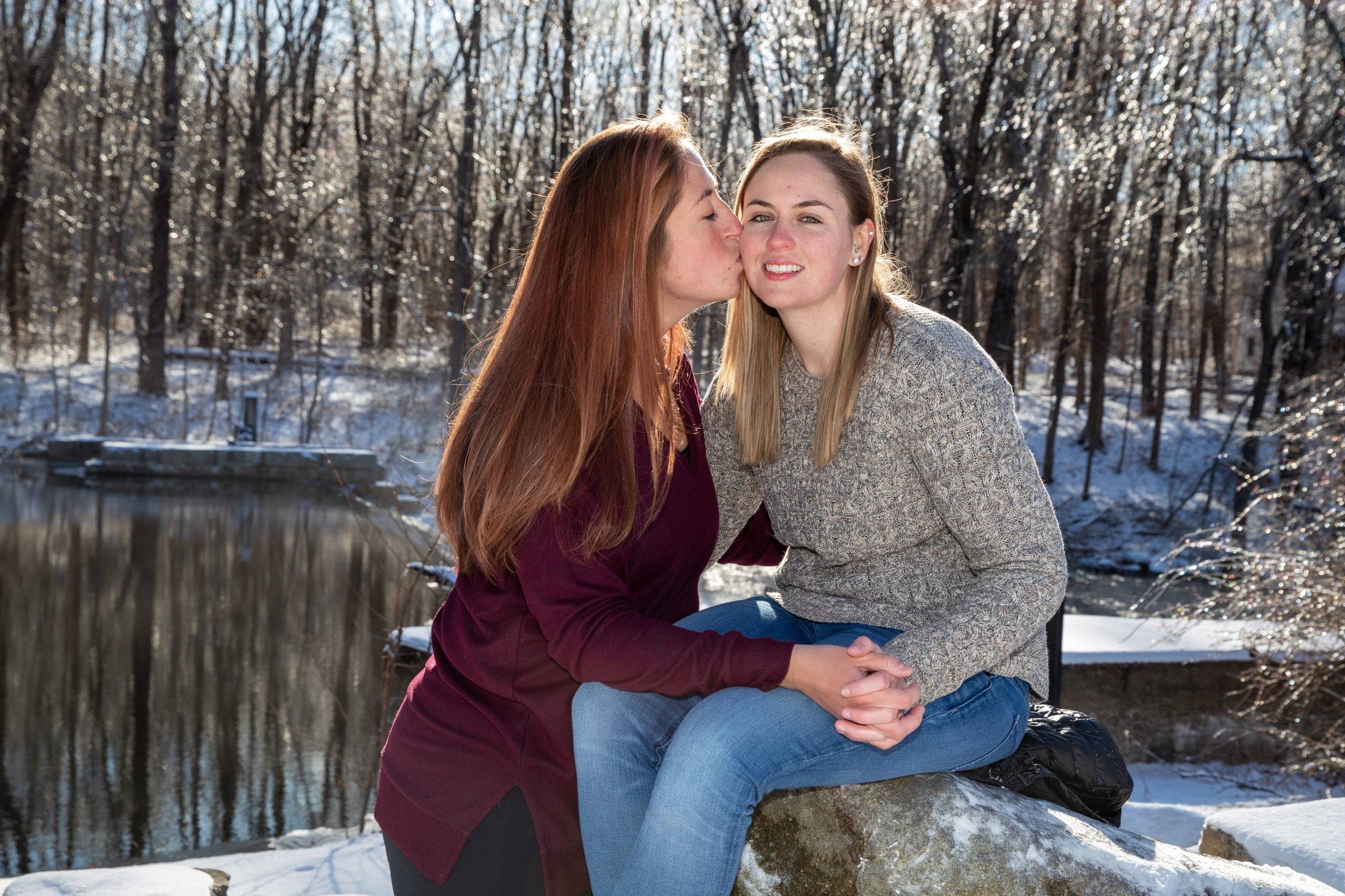 Two women sitting on a rock and kissing in the snow.