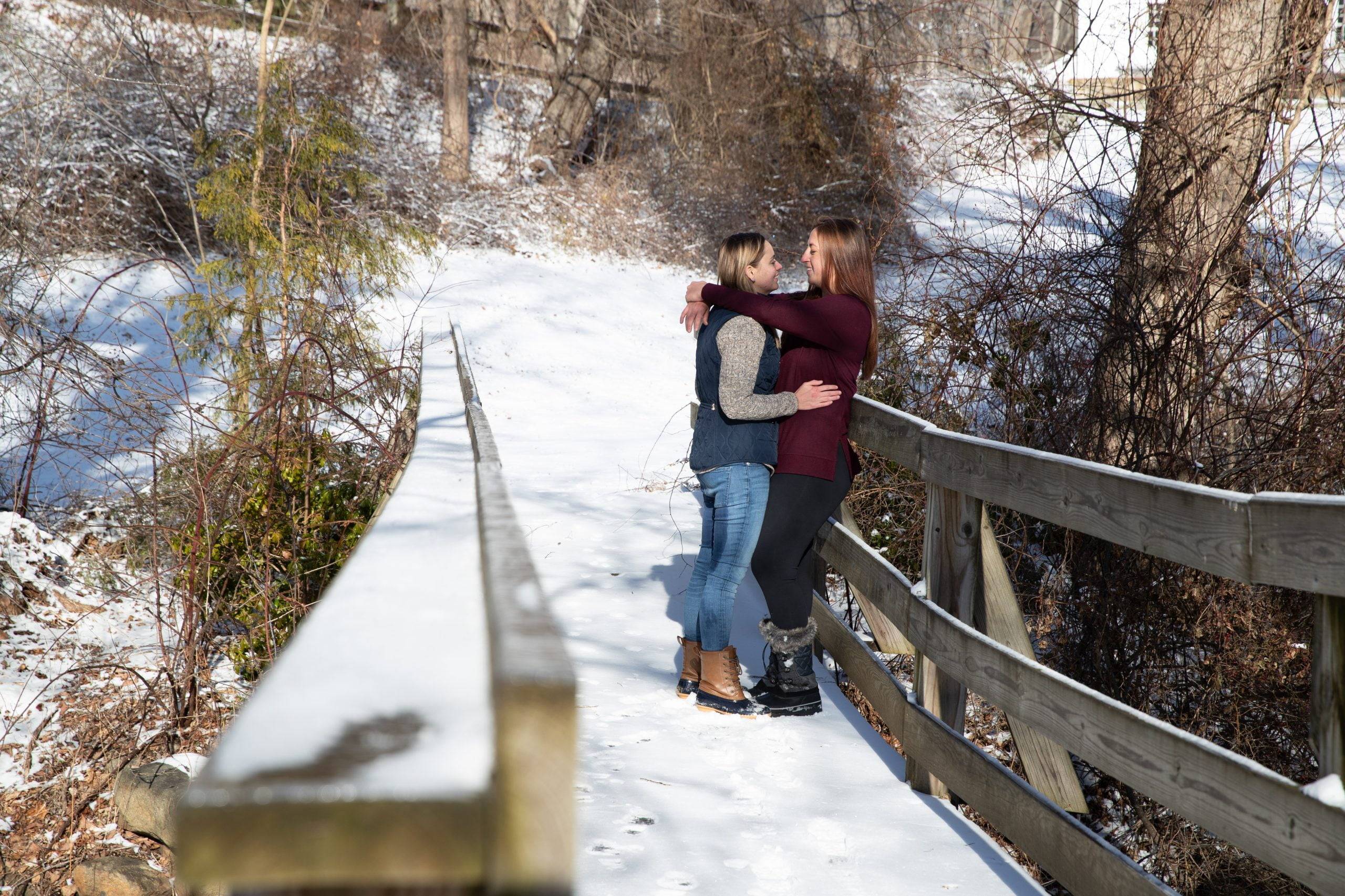 Two people hugging on a wooden bridge in the snow.