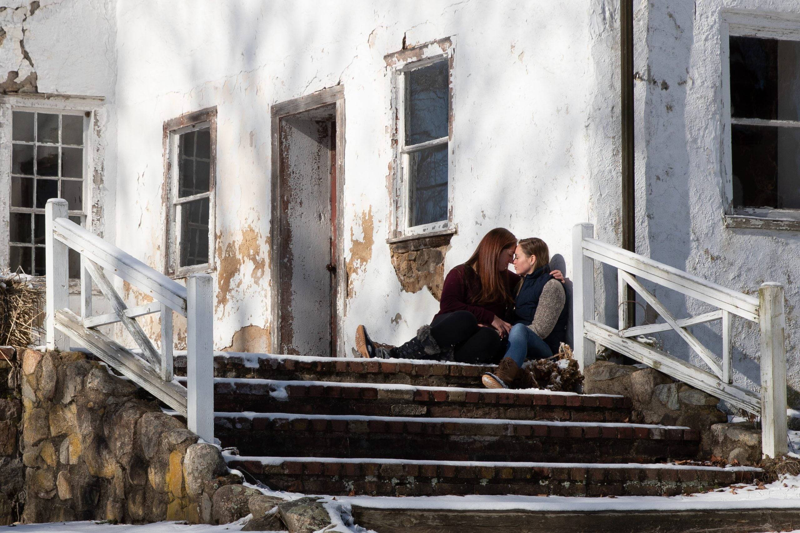 A couple sits on the steps of a building in the snow.