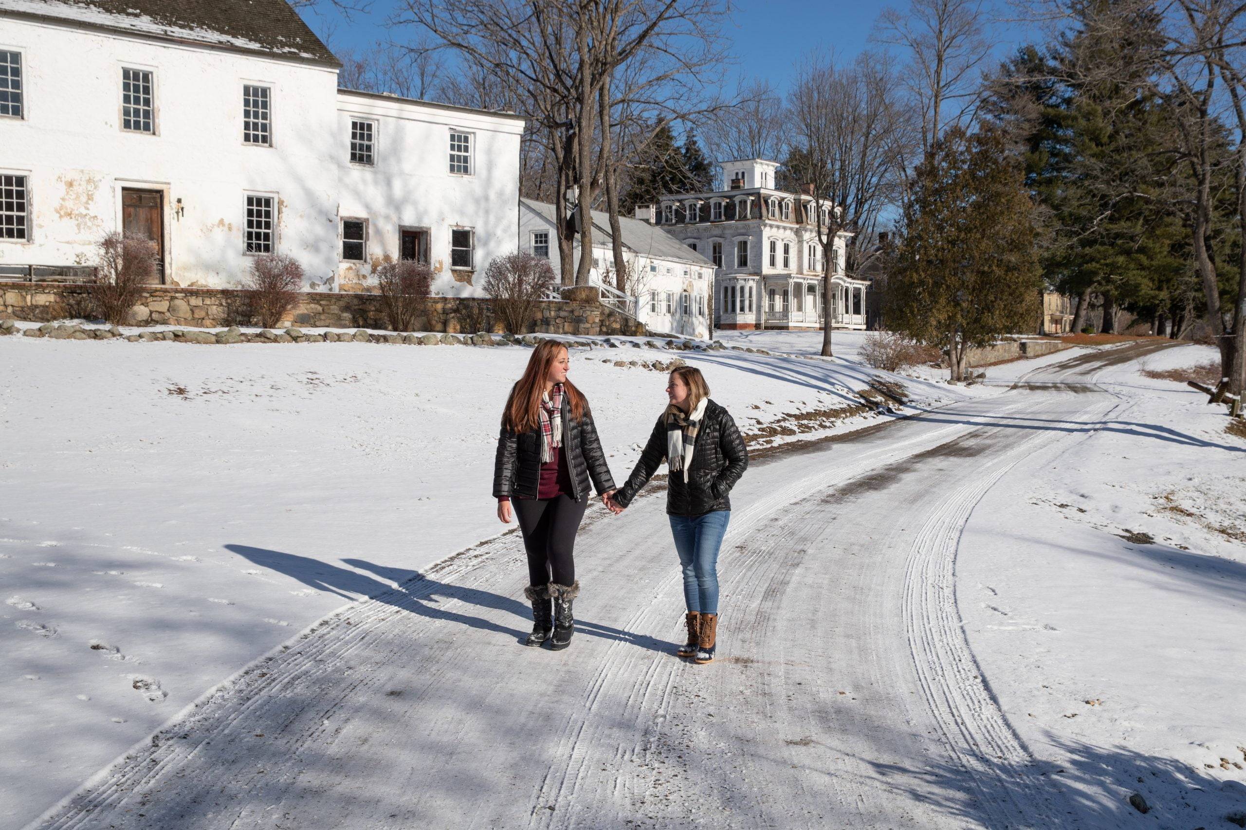 Two women walking down a snowy road in front of a house.