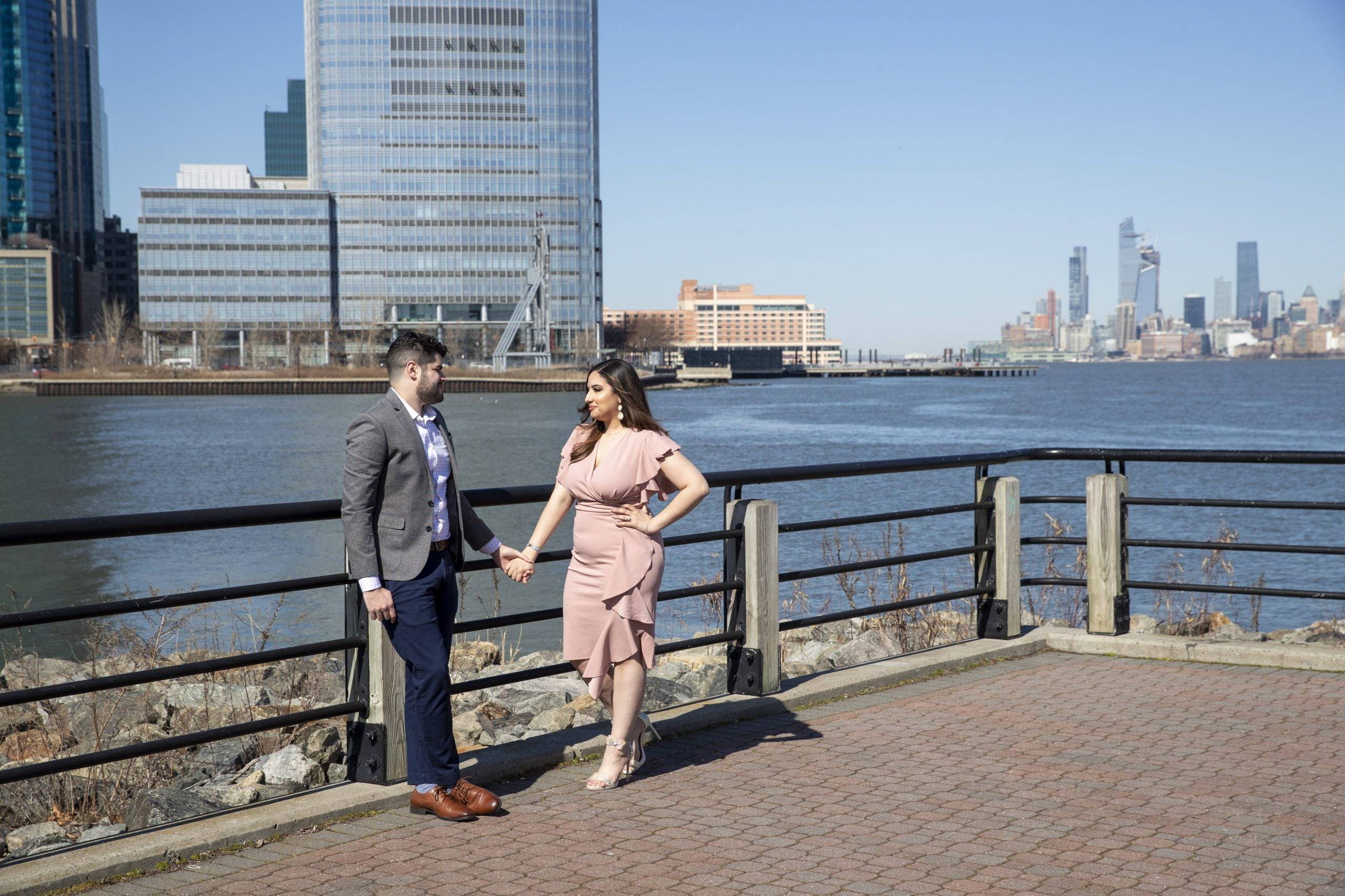 A couple standing on a bridge with the city skyline in the background.
