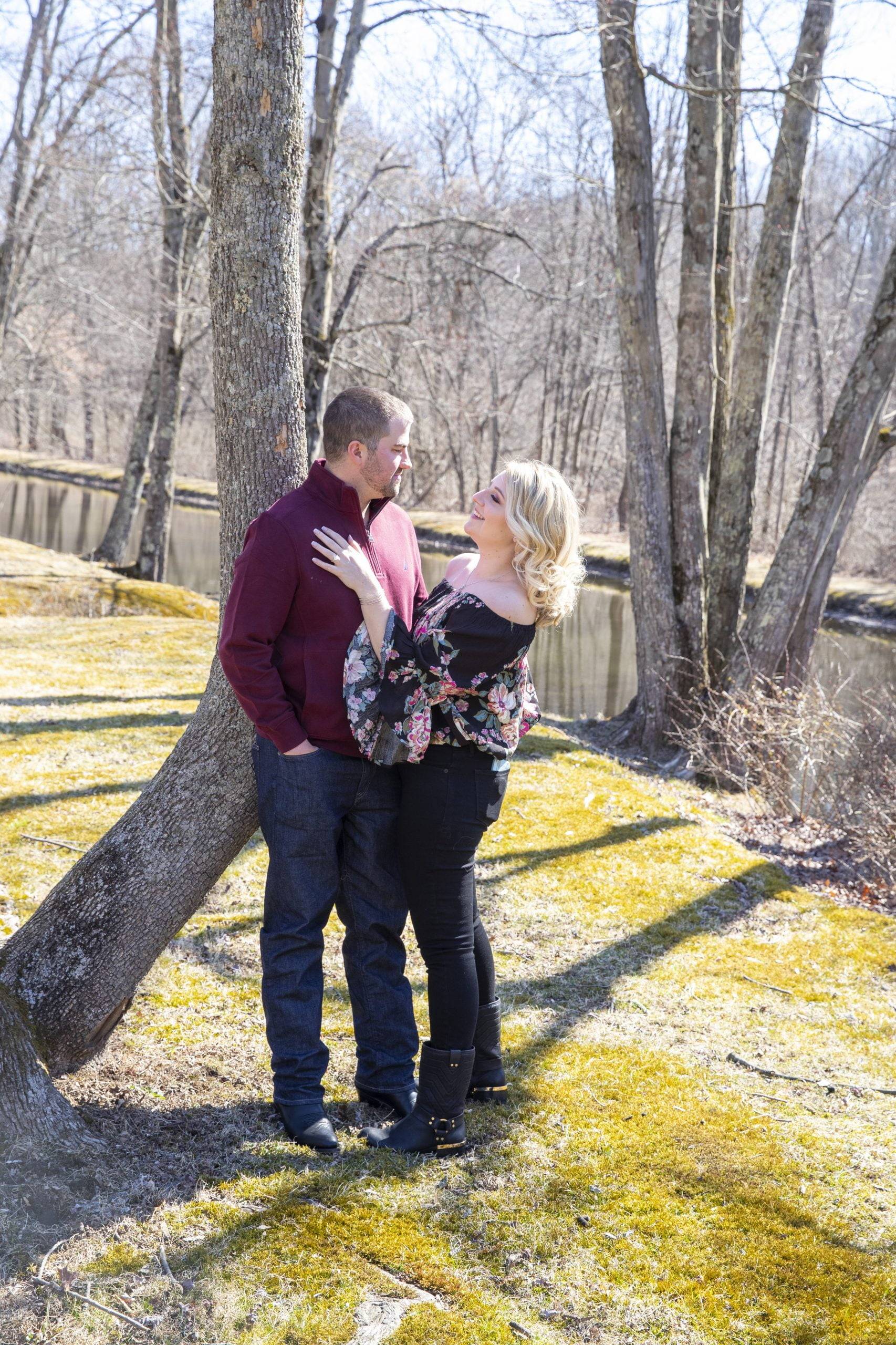 An engaged couple standing next to a tree in a park.
